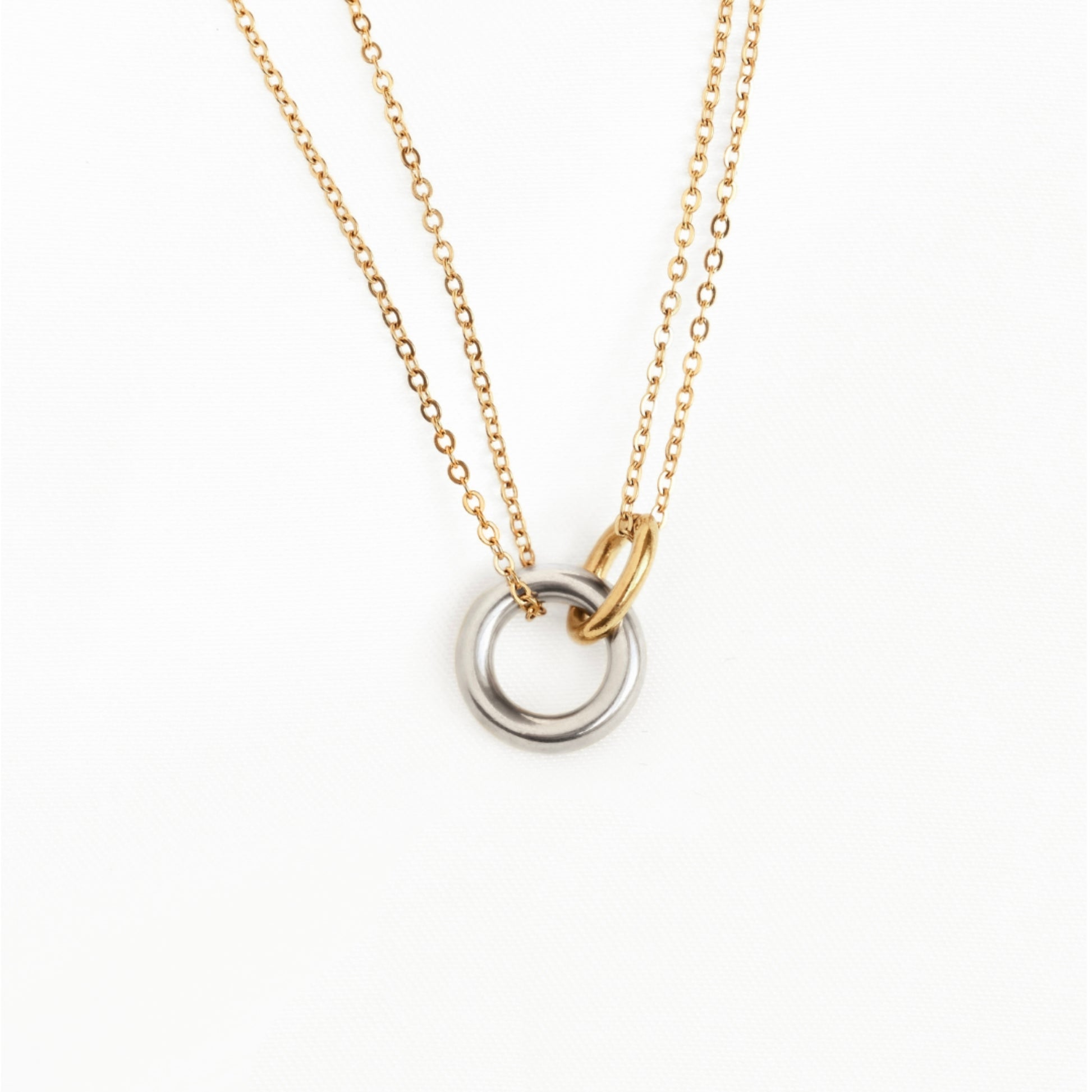 A delicate two-tone necklace featuring a fine gold cable chain, a small gold ring connector, and a double-ring pendant with one polished gold ring and one silver-toned ring, set against a plain white background.