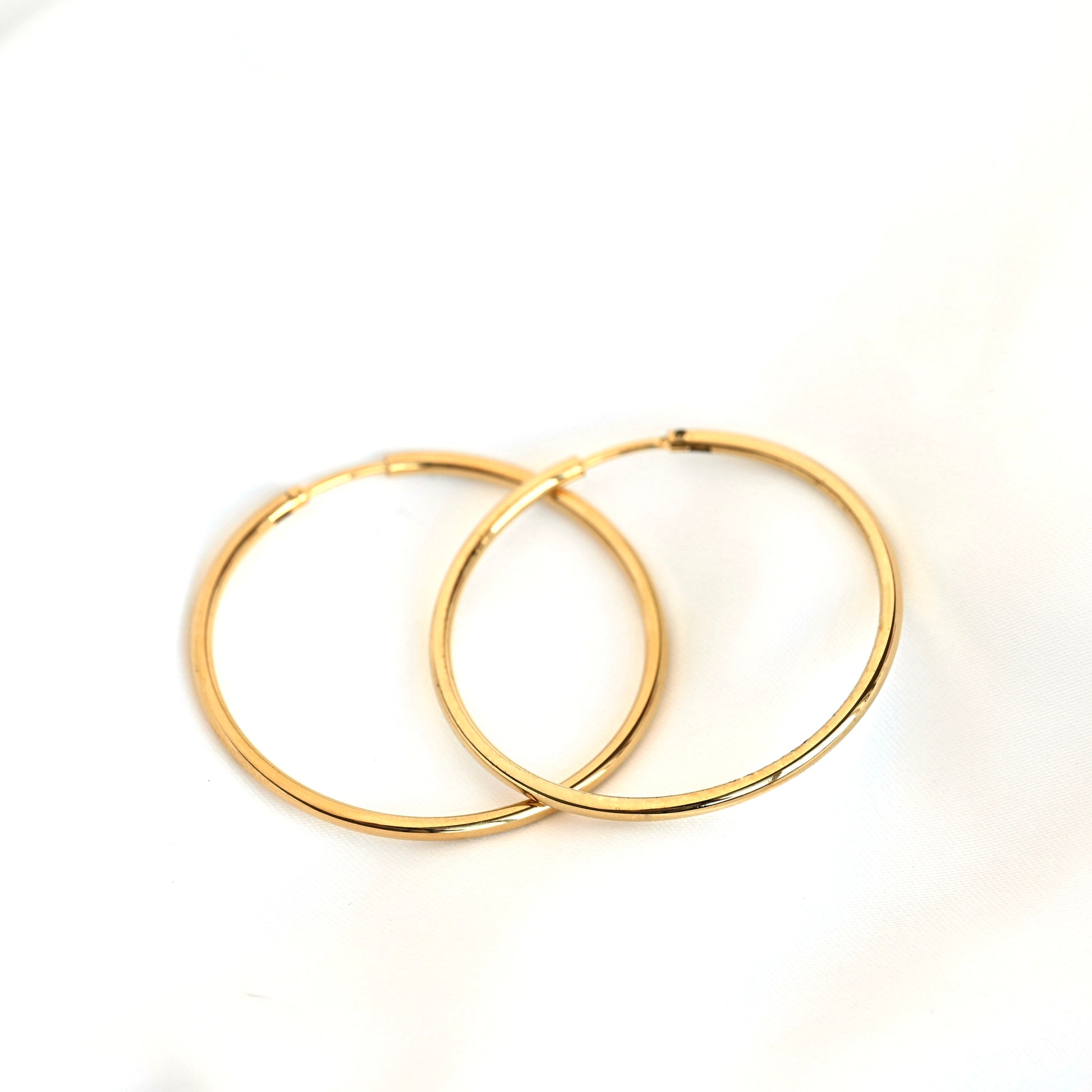A pair of thin endless gold hoop earrings overlapping on a plain white background.