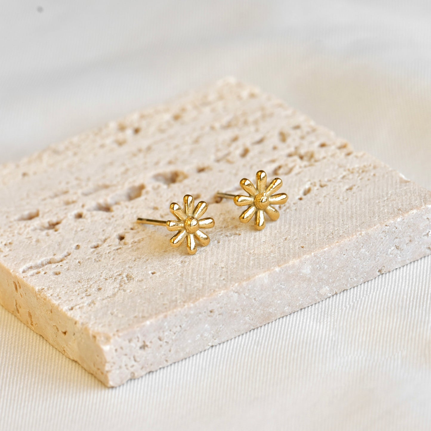 Gold flower-shaped earrings on a textured white surface