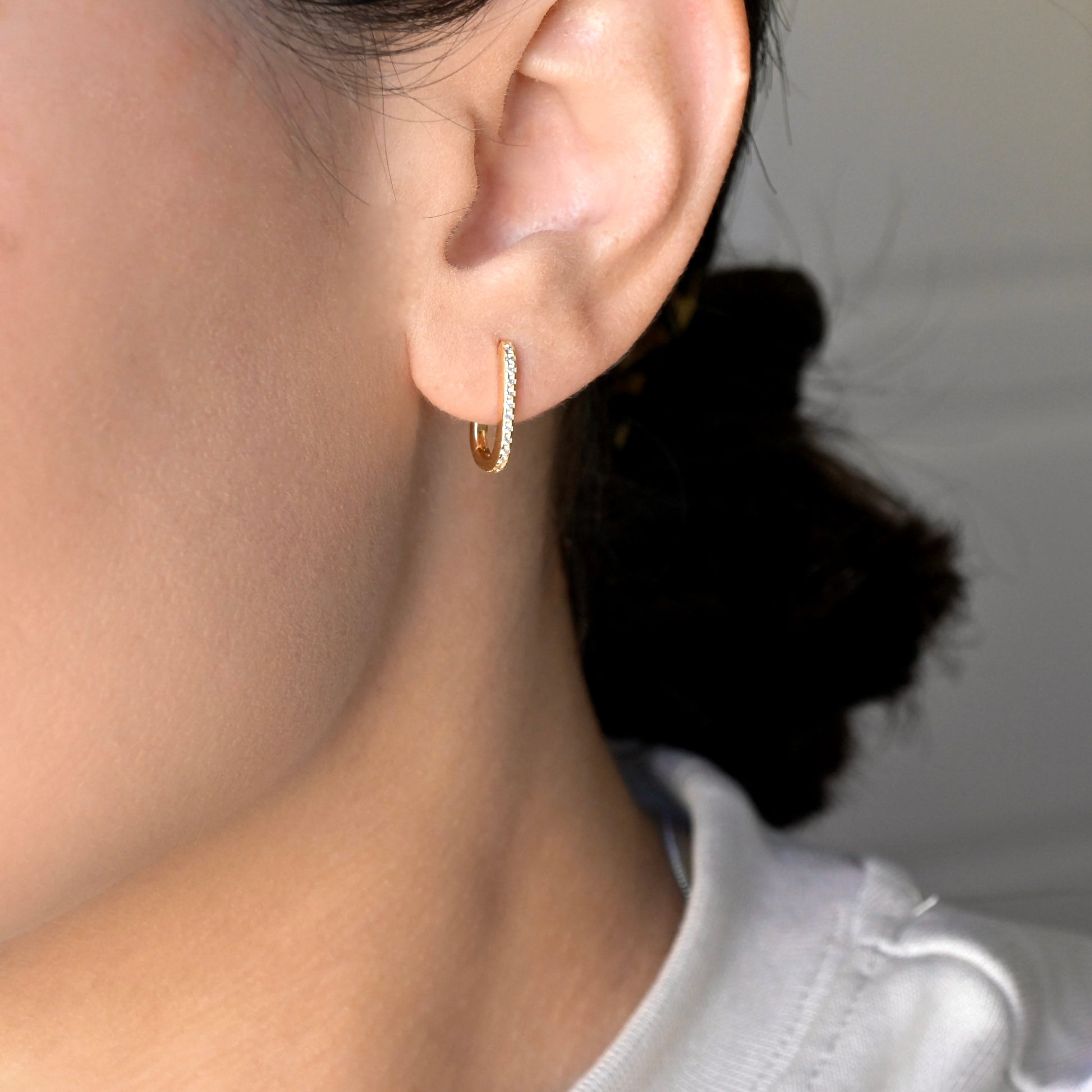 Close-up of an ear wearing a gold oblong hoop earring with a blurred background