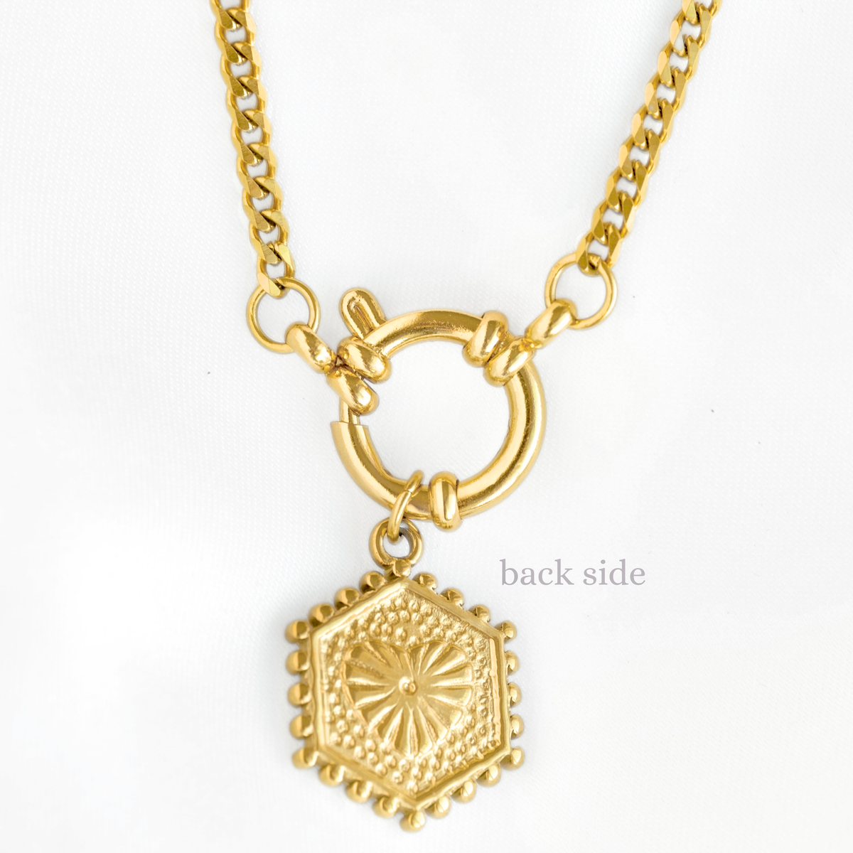 A gold-tone necklace with a hexagonal pendant featuring a sunburst pattern and beaded border, suspended from a curb chain with a toggle clasp, shown on a white background with the text 'back side' indicating the reverse side of the pendant.