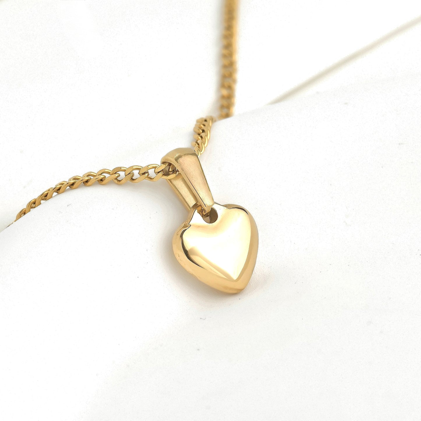 Gold curb chain necklace with a small flat heart pendant against a white background