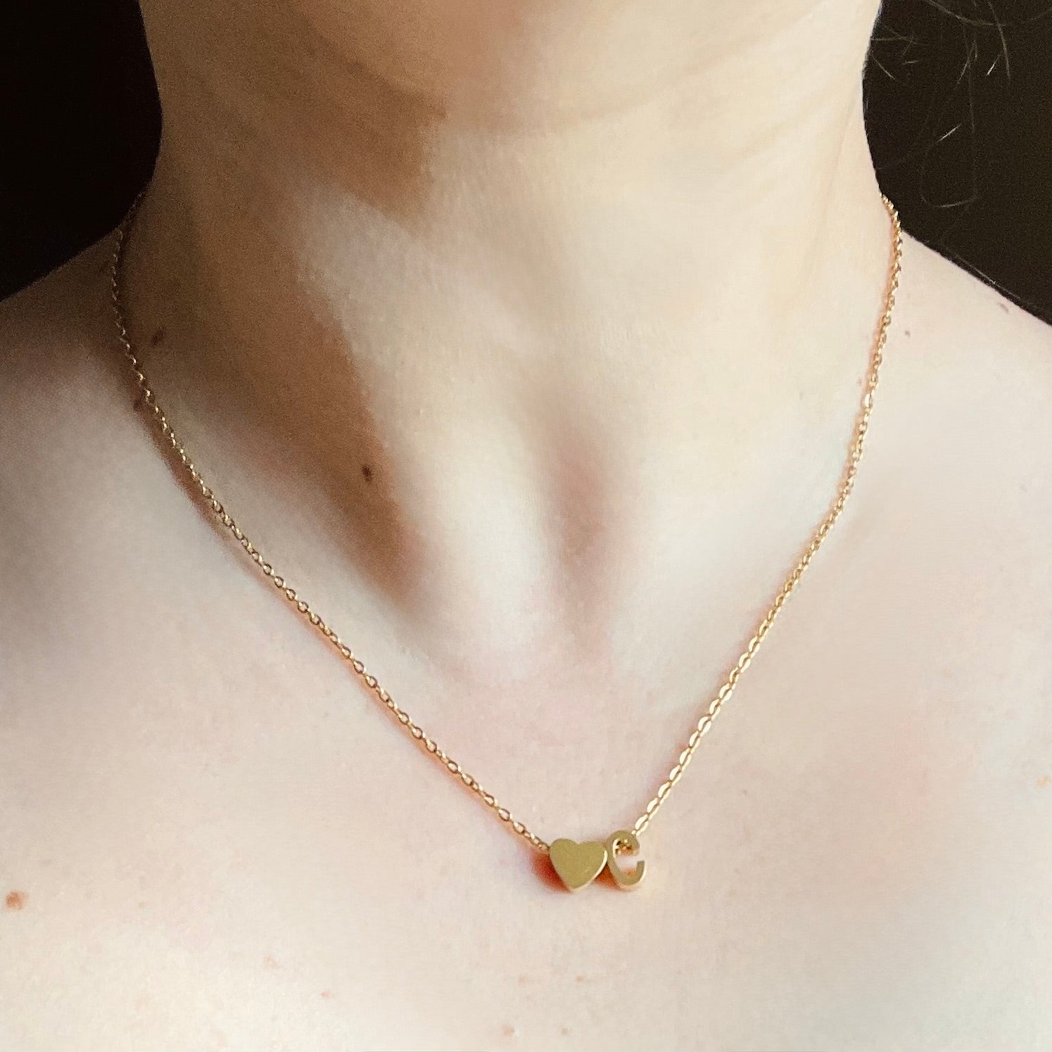 Gold necklace with a heart and initial pendant on a person's neck