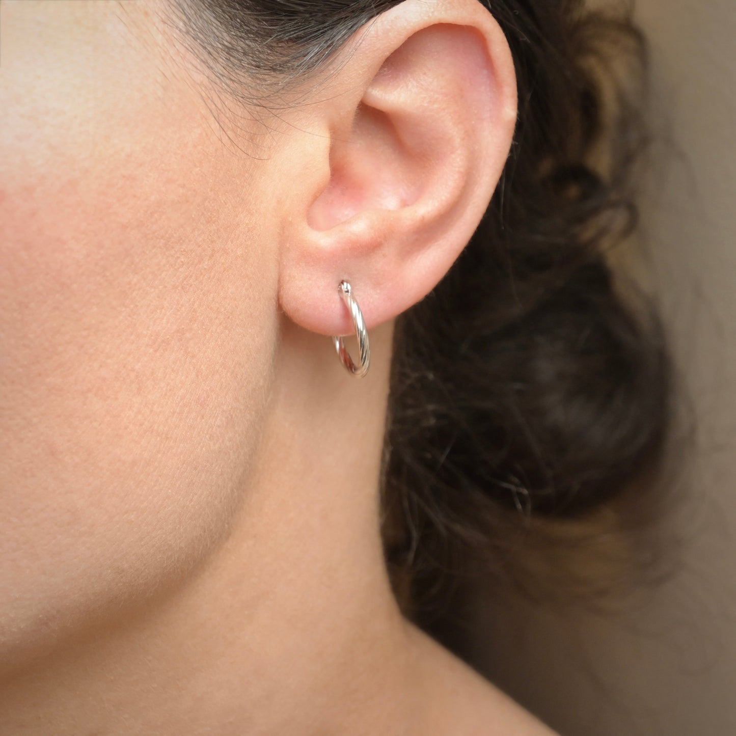 Close-up of an ear wearing a silver rope hoops with a neutral background