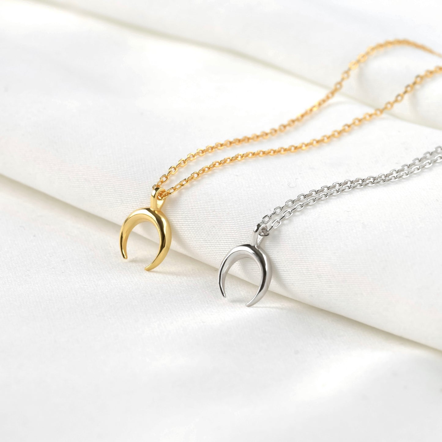 Gold and silver crescent moon necklaces on a white surface