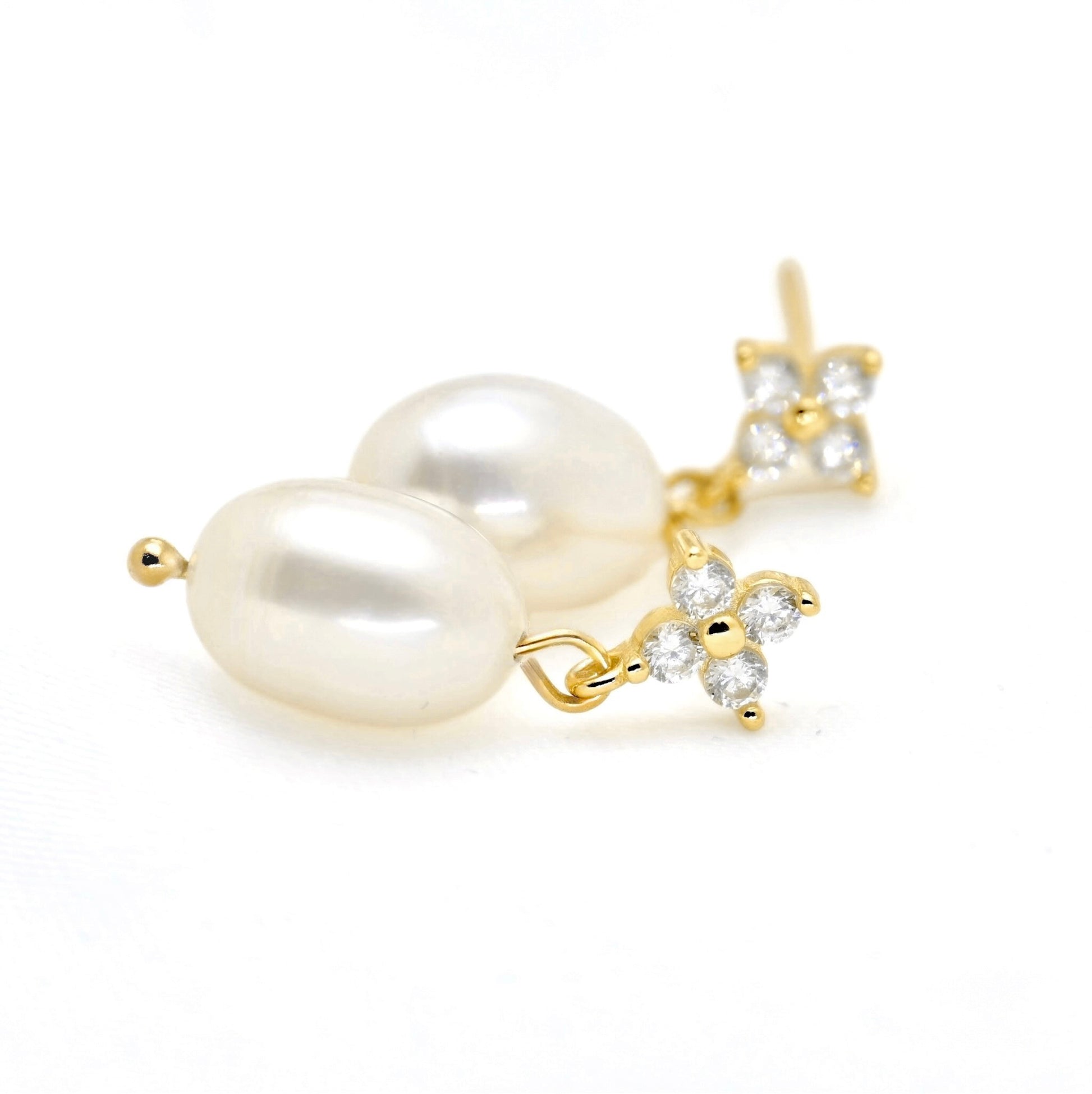 A pair of gold-plated dangle earrings featuring large, lustrous baroque pearls and small flower-shaped clusters of clear cubic zirconia stones, set against a plain white background.