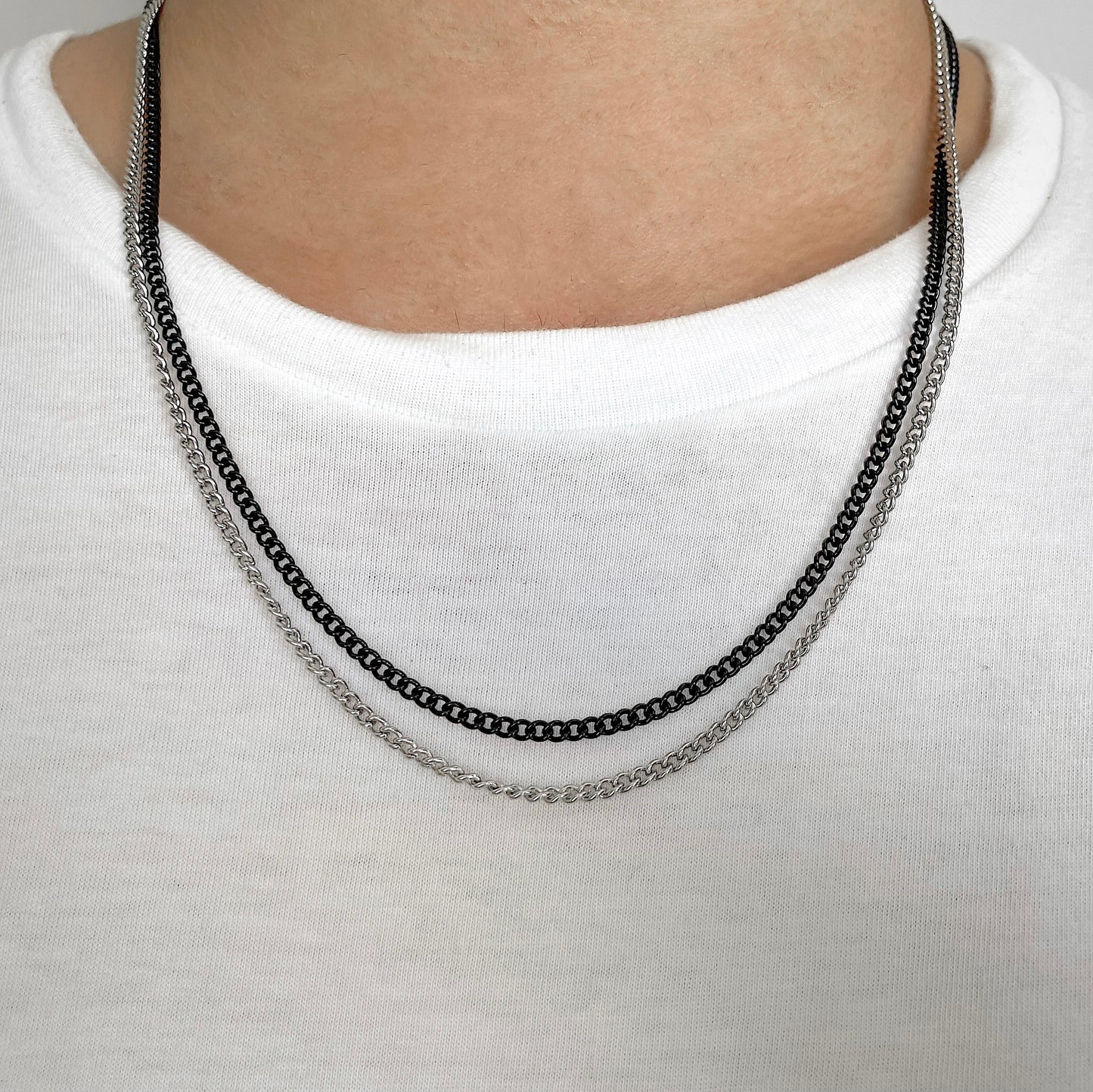 Silver and black curb chain necklace on a man wearing a white shirt