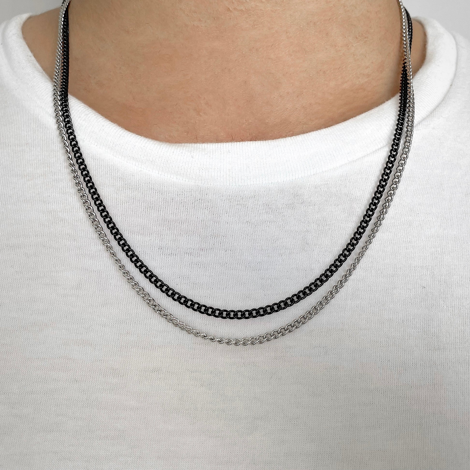 Silver and black curb chain necklace on a man wearing a white shirt
