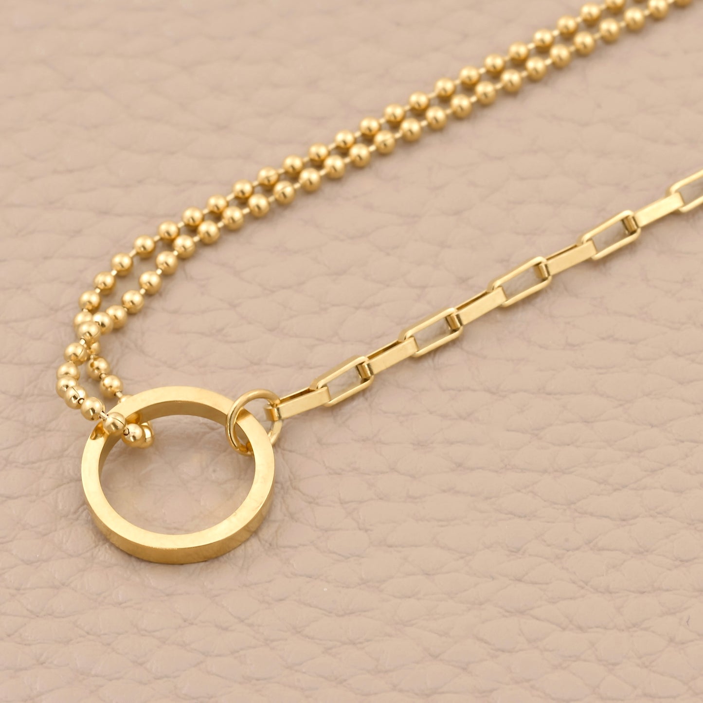 Gold bracelet with a circular pendant on a beige background