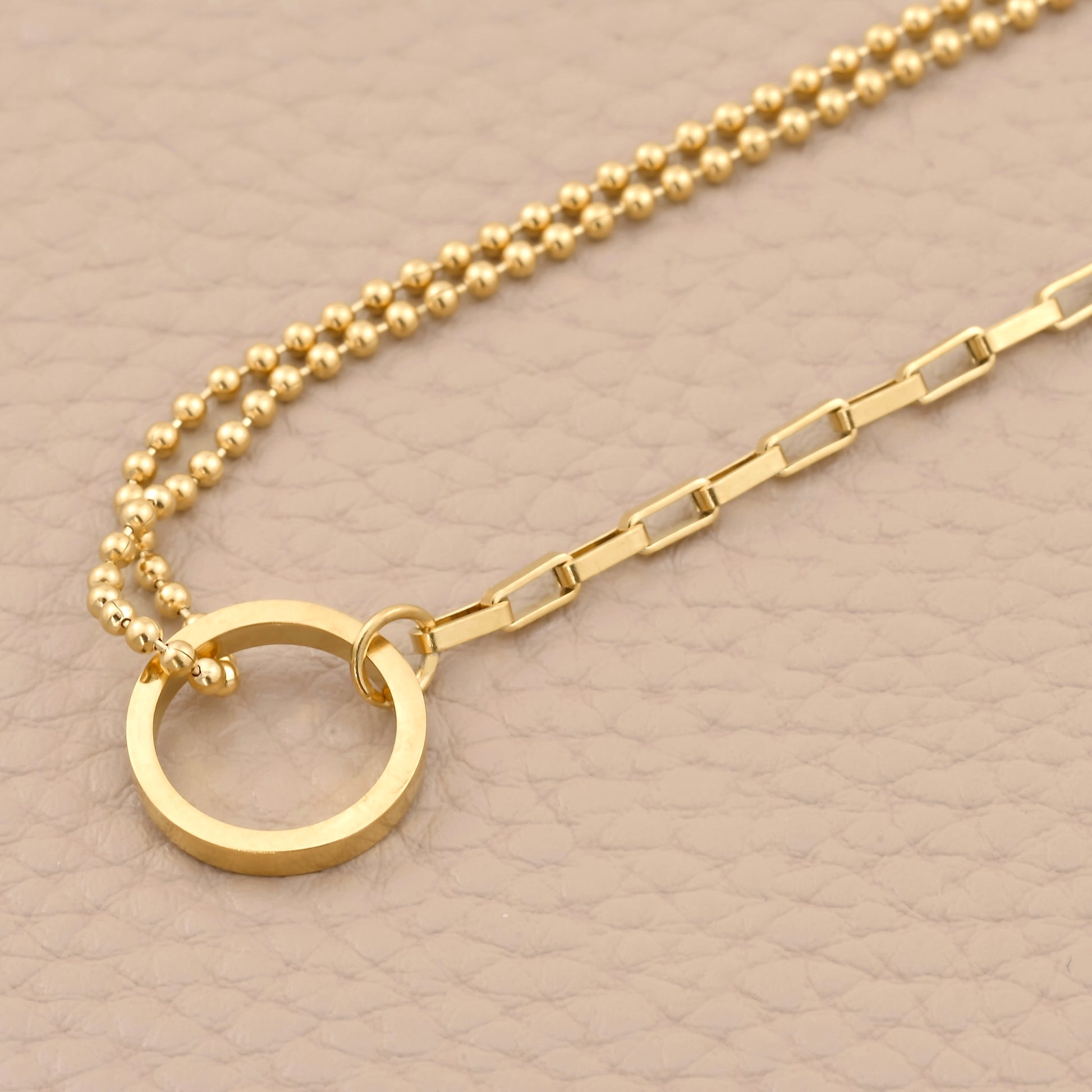 Gold bracelet with a circular pendant on a beige background