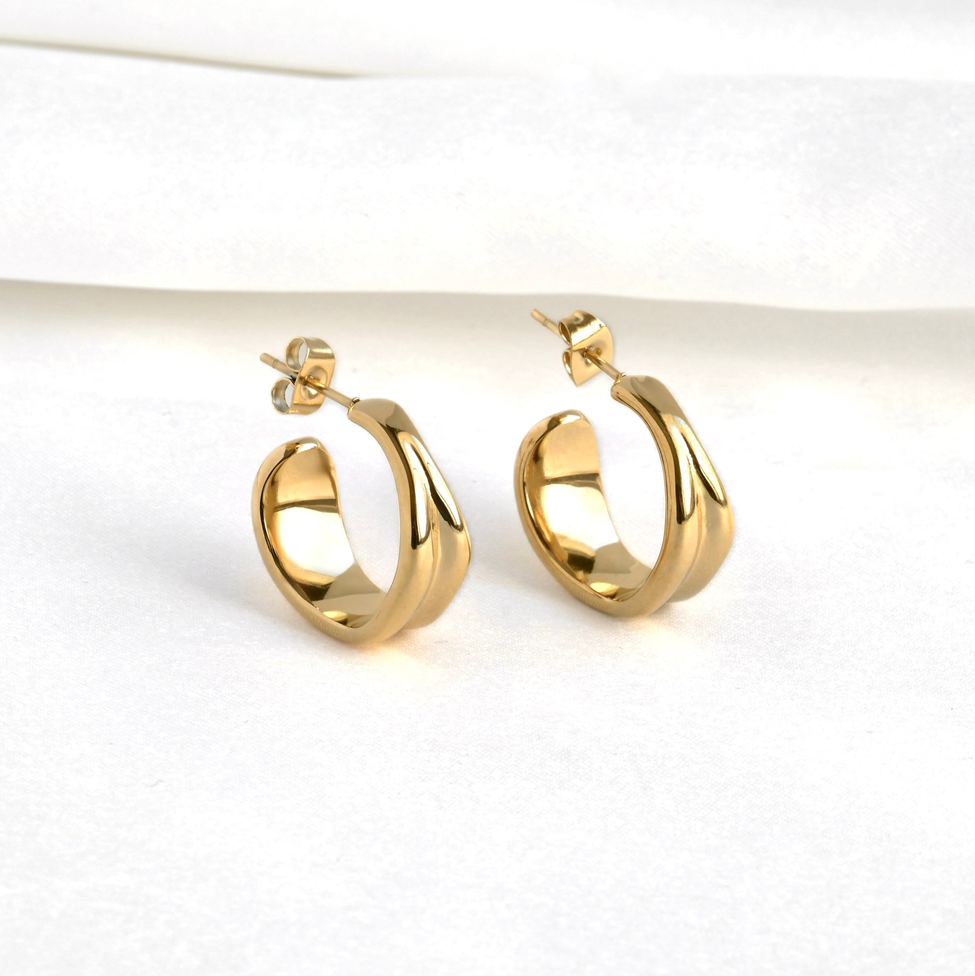 Gold crescent hoop earrings  with an irregular shape on a white background