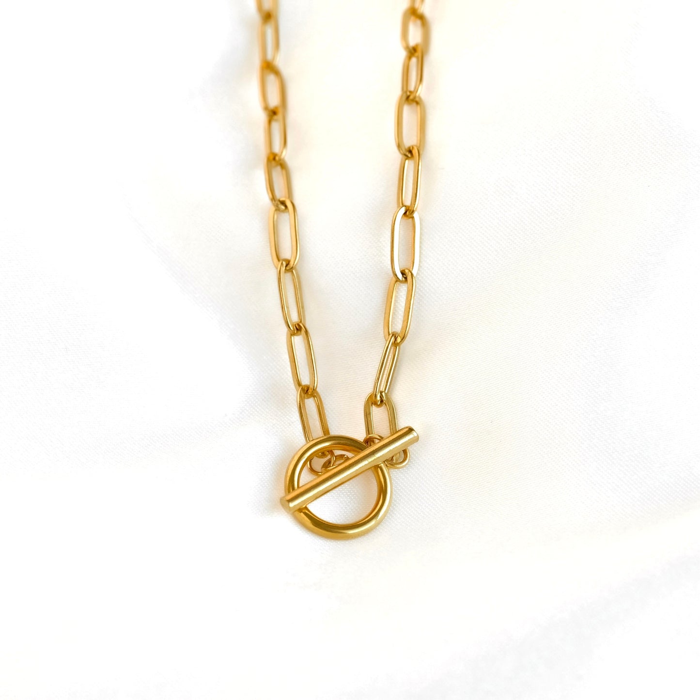 A gold paperclip chain necklace with a toggle ring clasp, photographed against a clean white background.