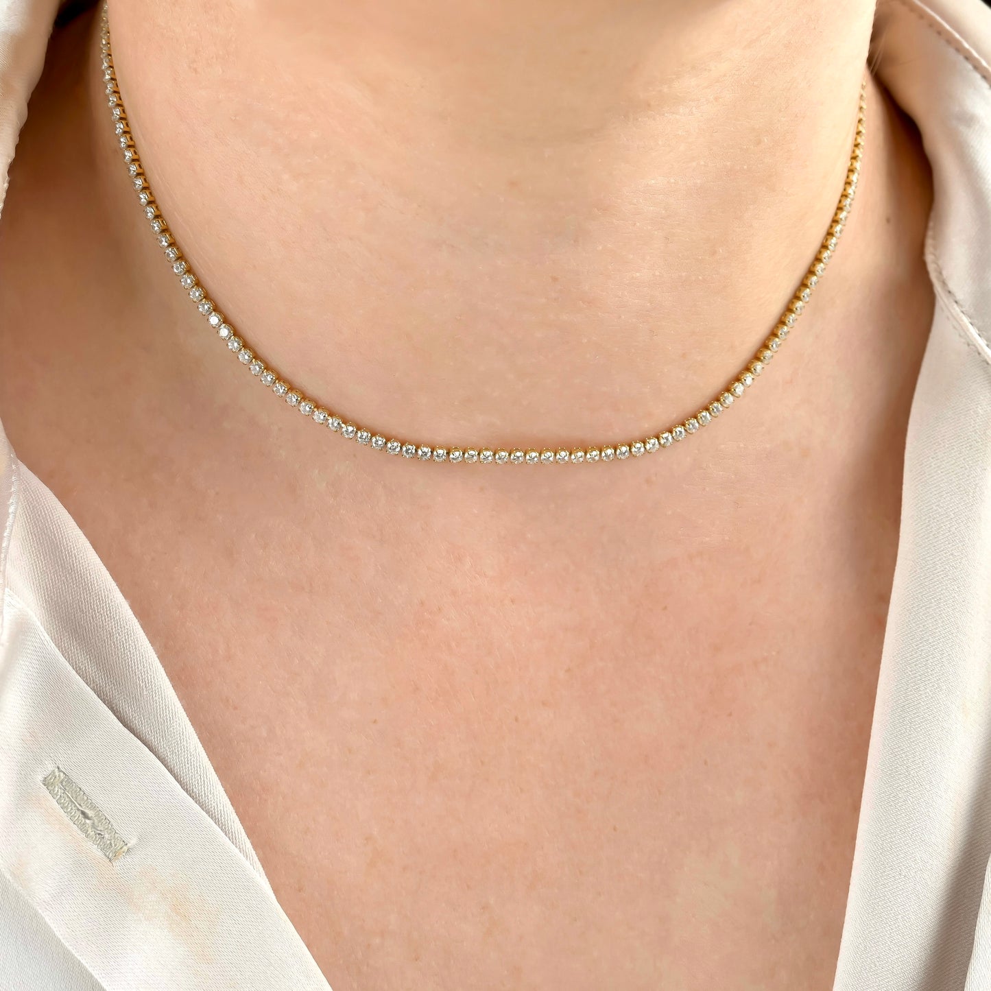 front view of gold tennis necklace with 2mm diamonds on a person wearing a white shirt.