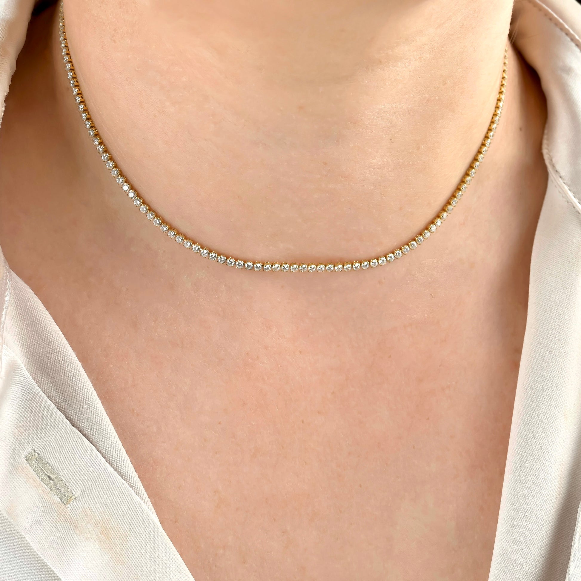 front view of gold tennis necklace with 2mm diamonds on a person wearing a white shirt.