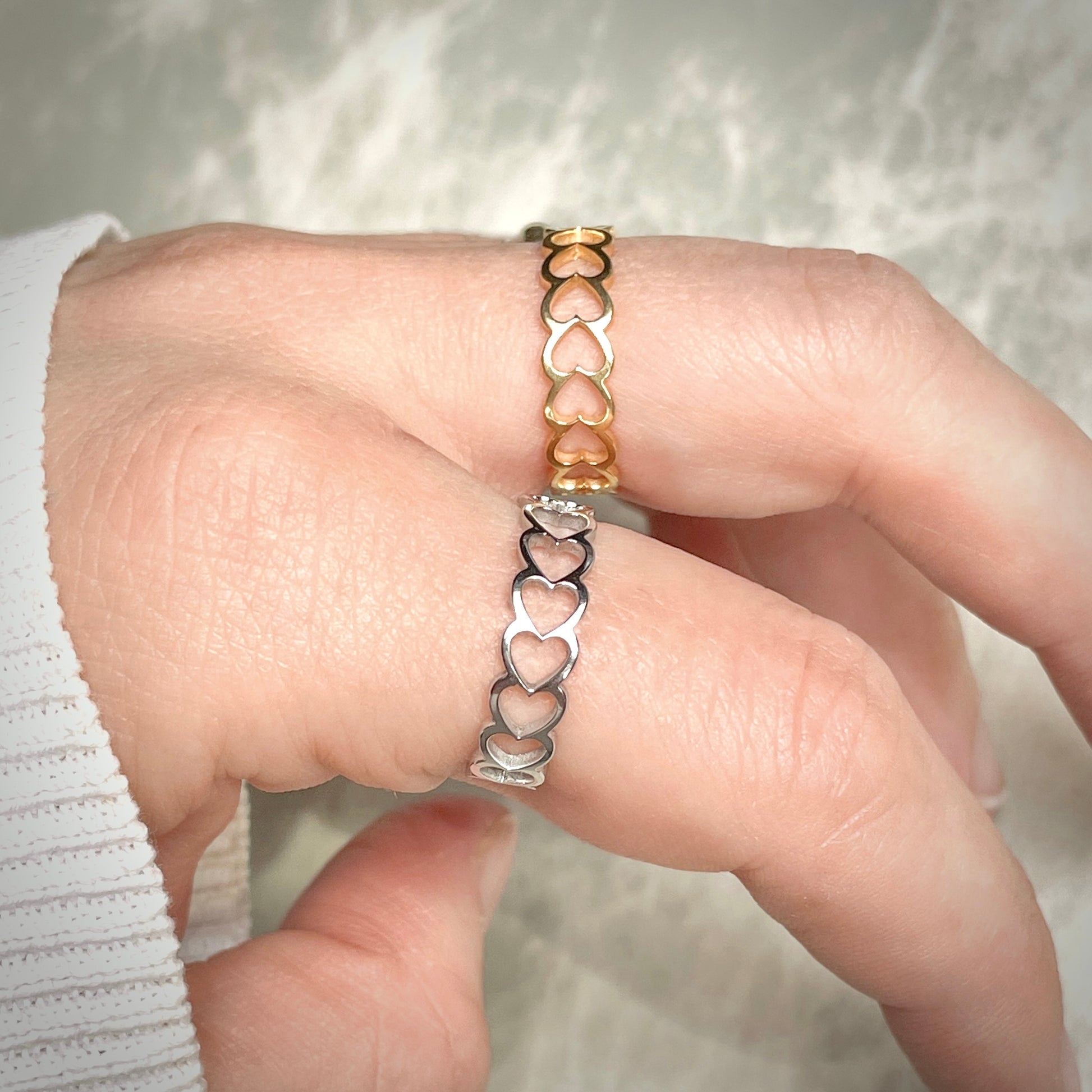 One gold and one silver heart-shaped ring on a finger with a blurred background