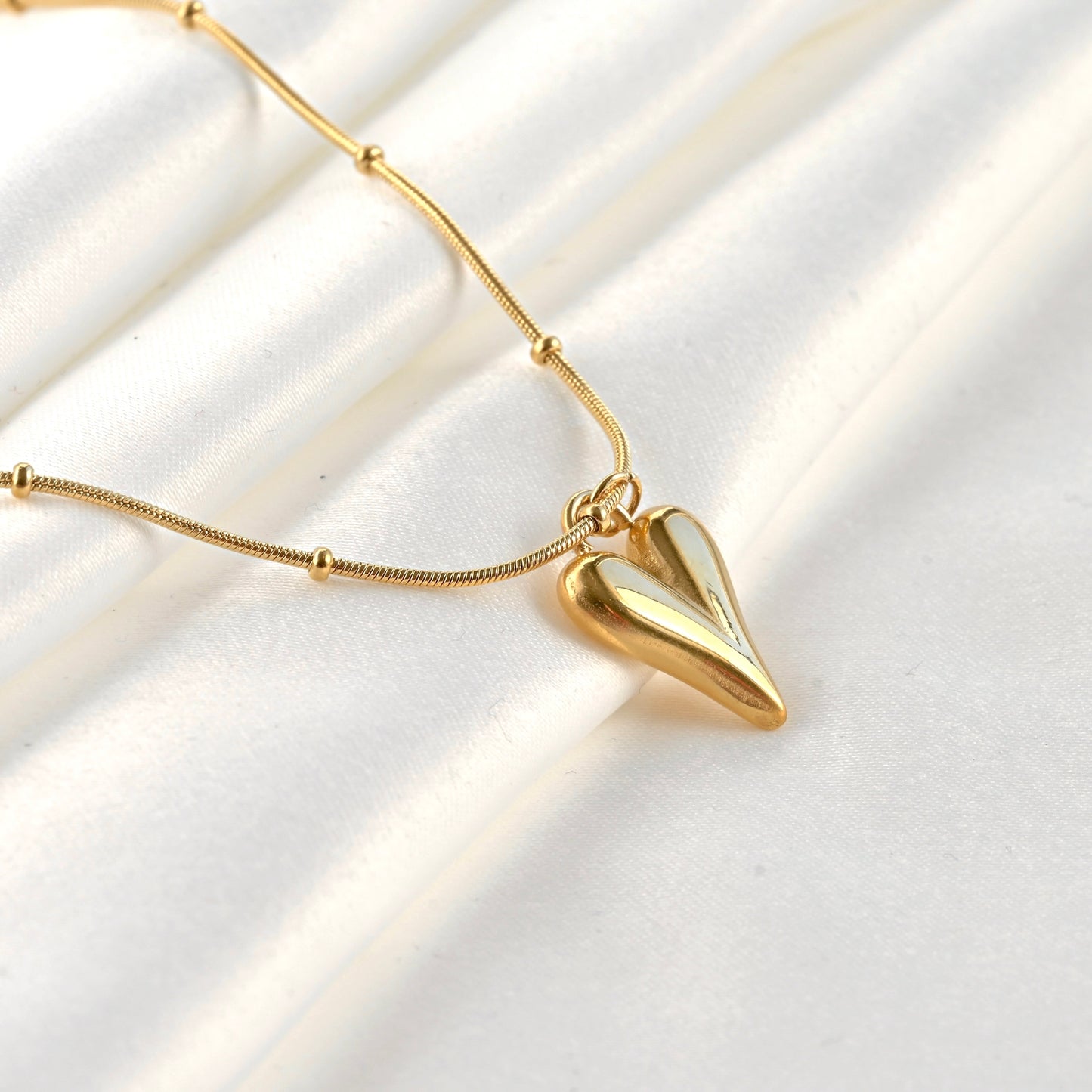 Side view of gold heart necklace with a beaded snake chain on a white background