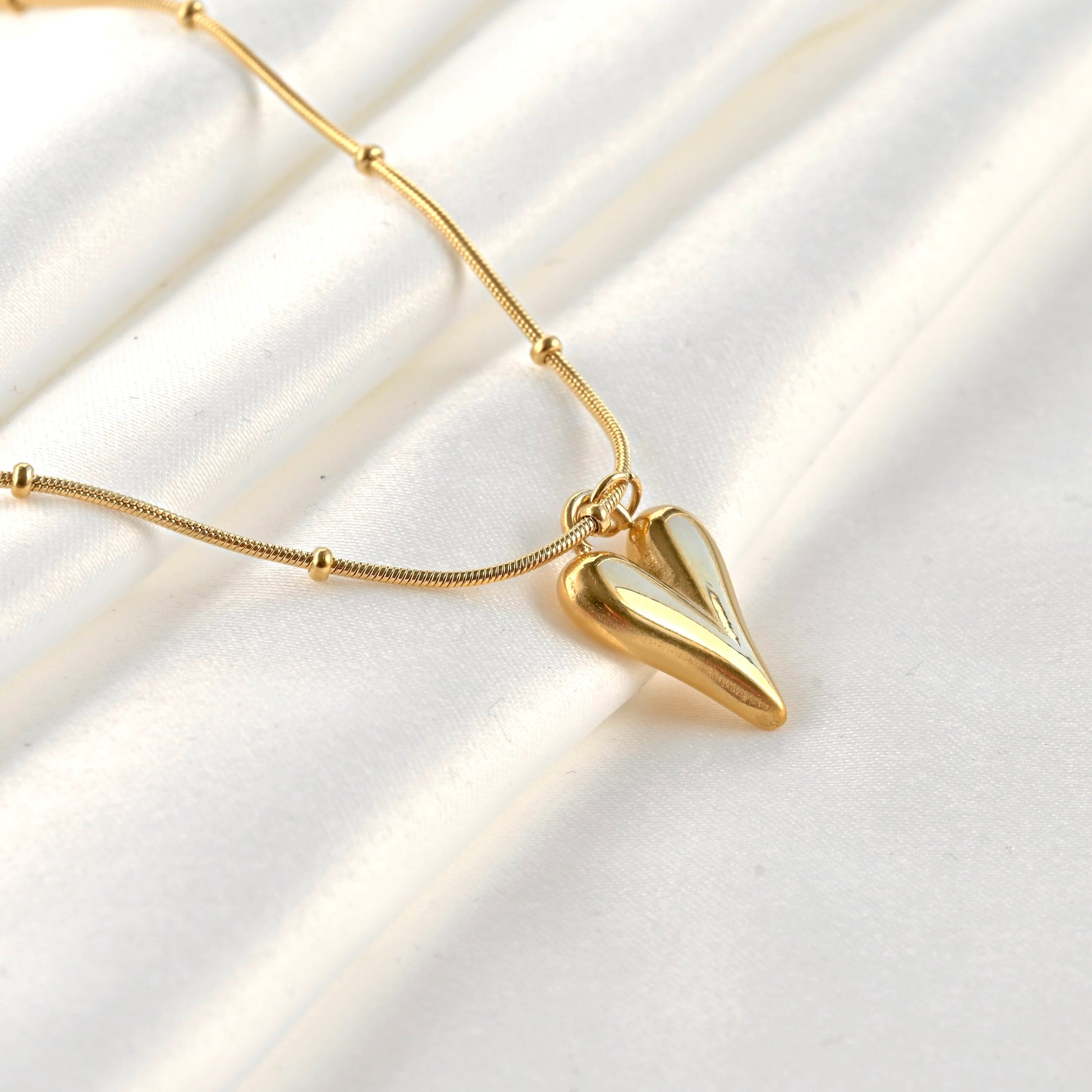 Side view of gold heart necklace with a beaded snake chain on a white background