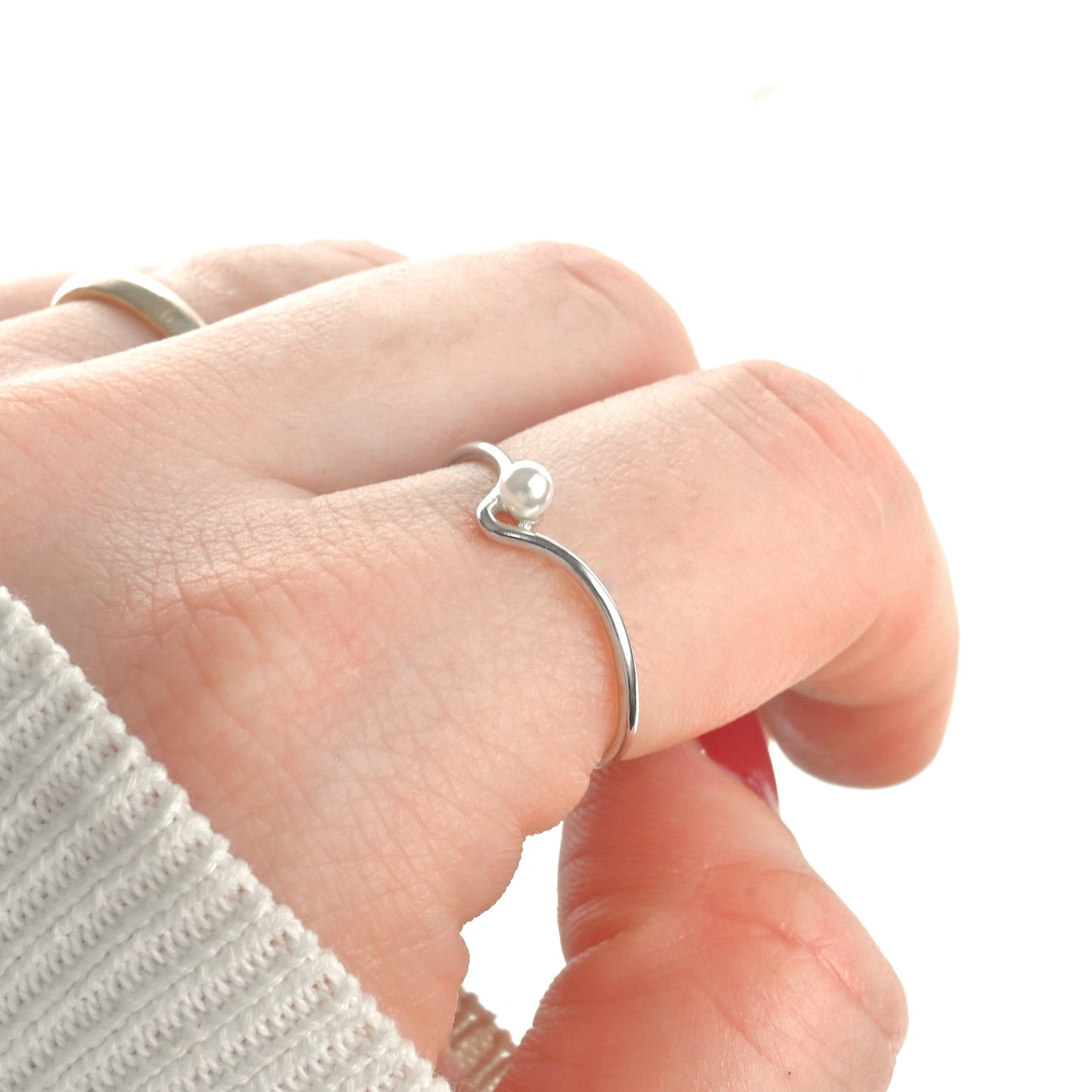 Silver ring with a small pearl on a finger against a white background