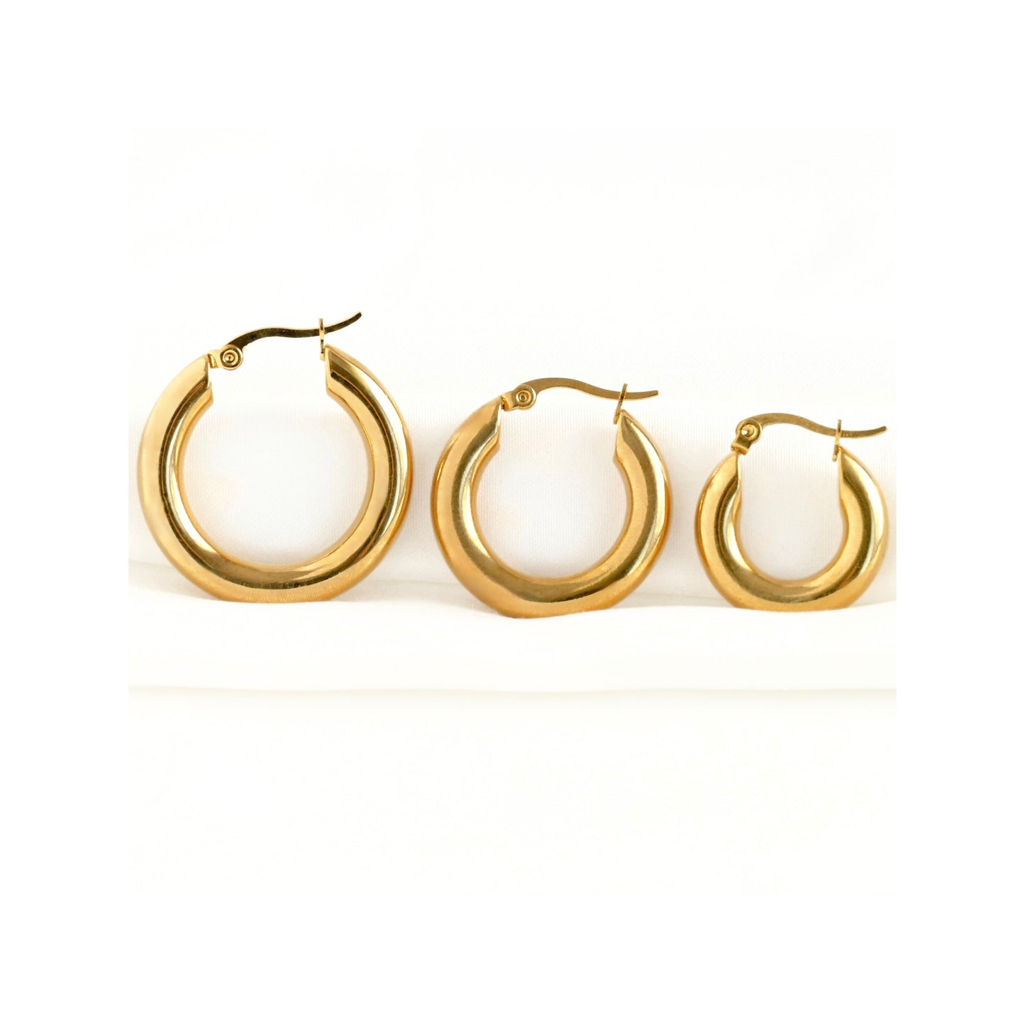 Three chunky gold hoop earrings of different sizes on a white background