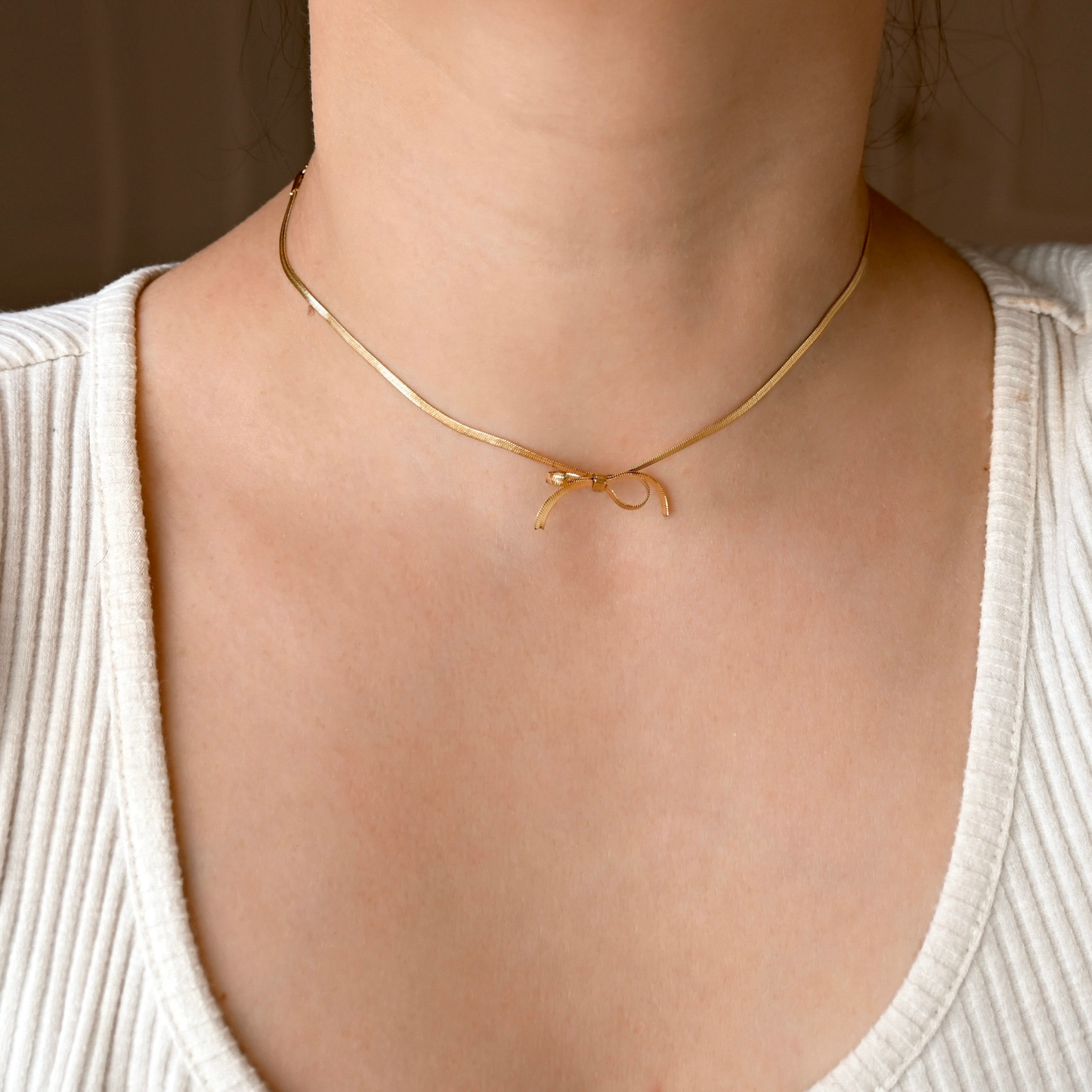 Front view of a person wearing a dainty gold herringbone necklace with a bowtie in the center made from the same chain