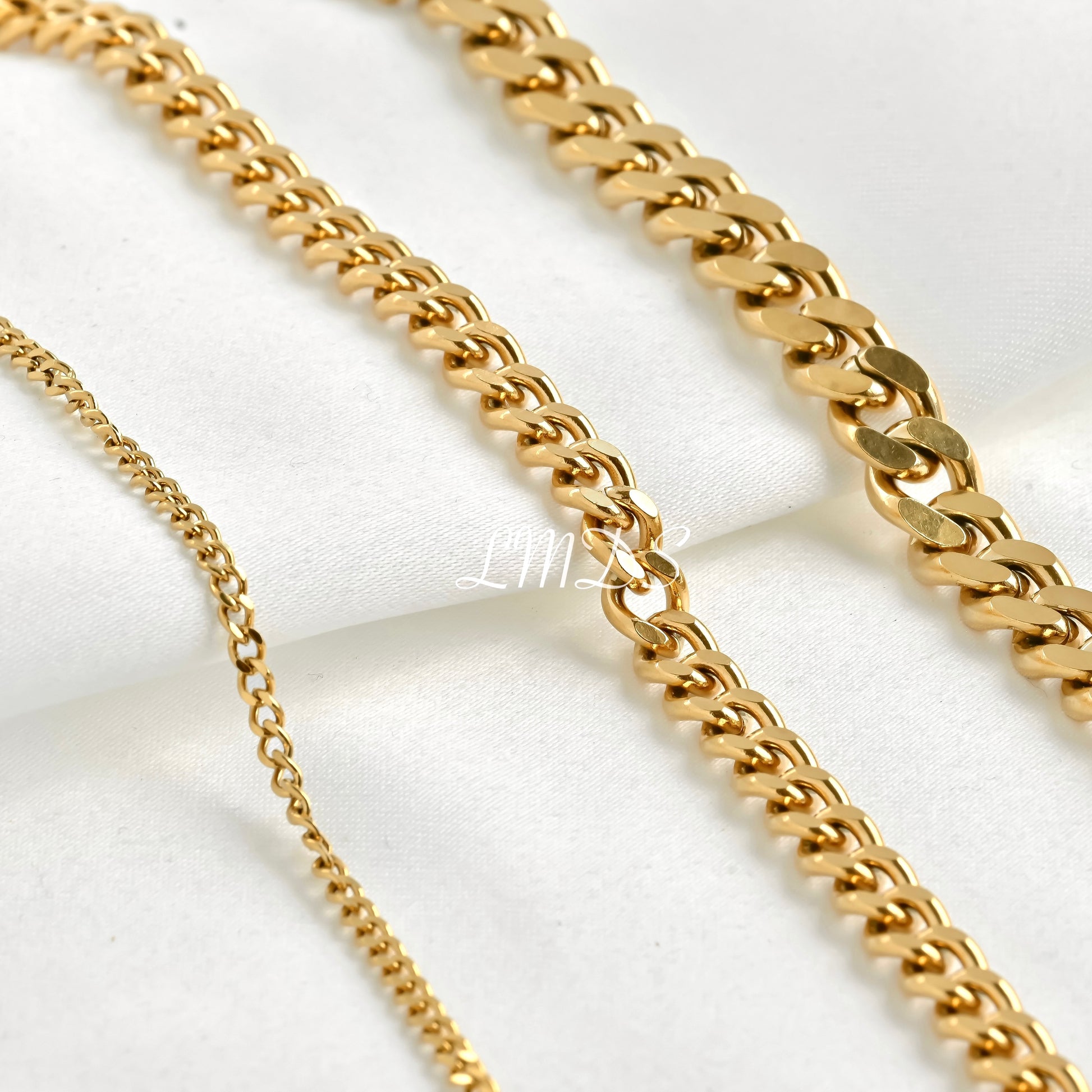 Close up view of dainty and chunky gold cuban chains on a white background