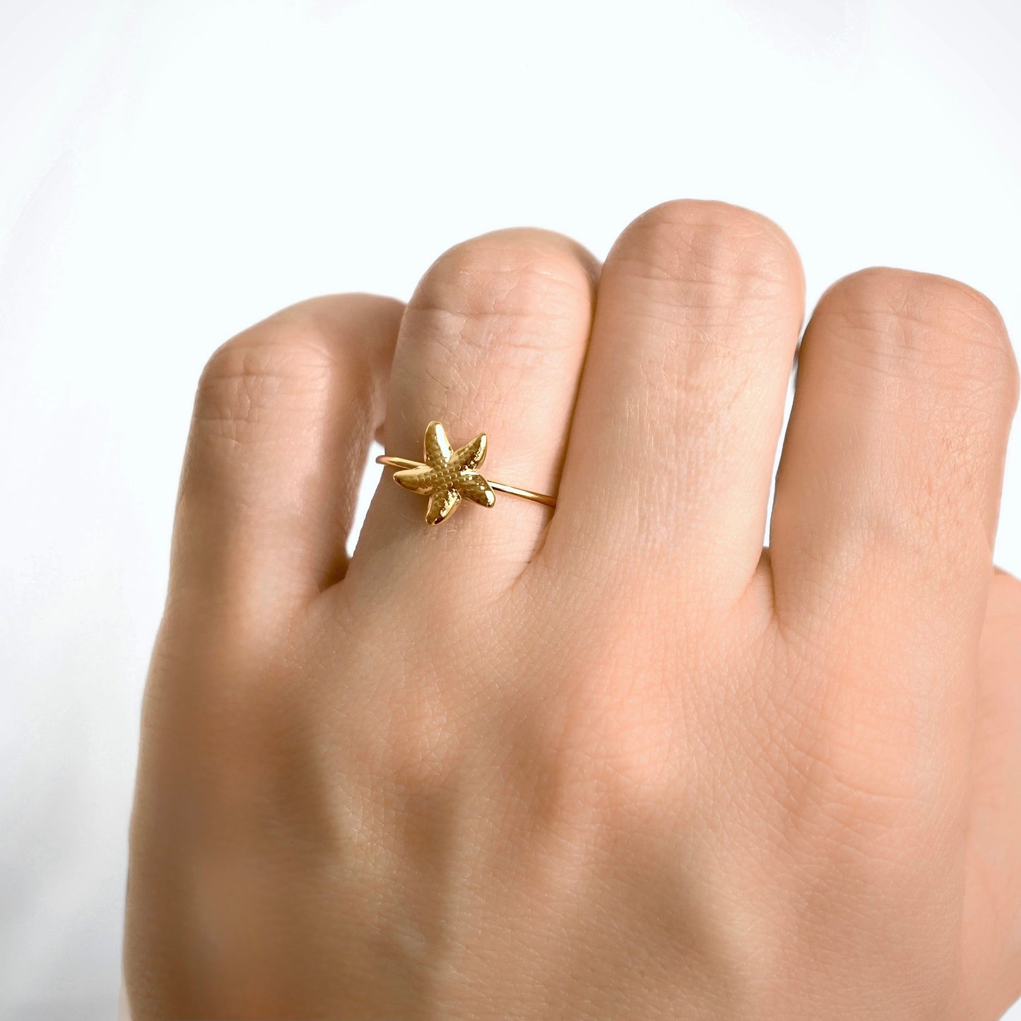A gold starfish ring worn on a person's ring finger, shown in a close-up shot against a clean white background.