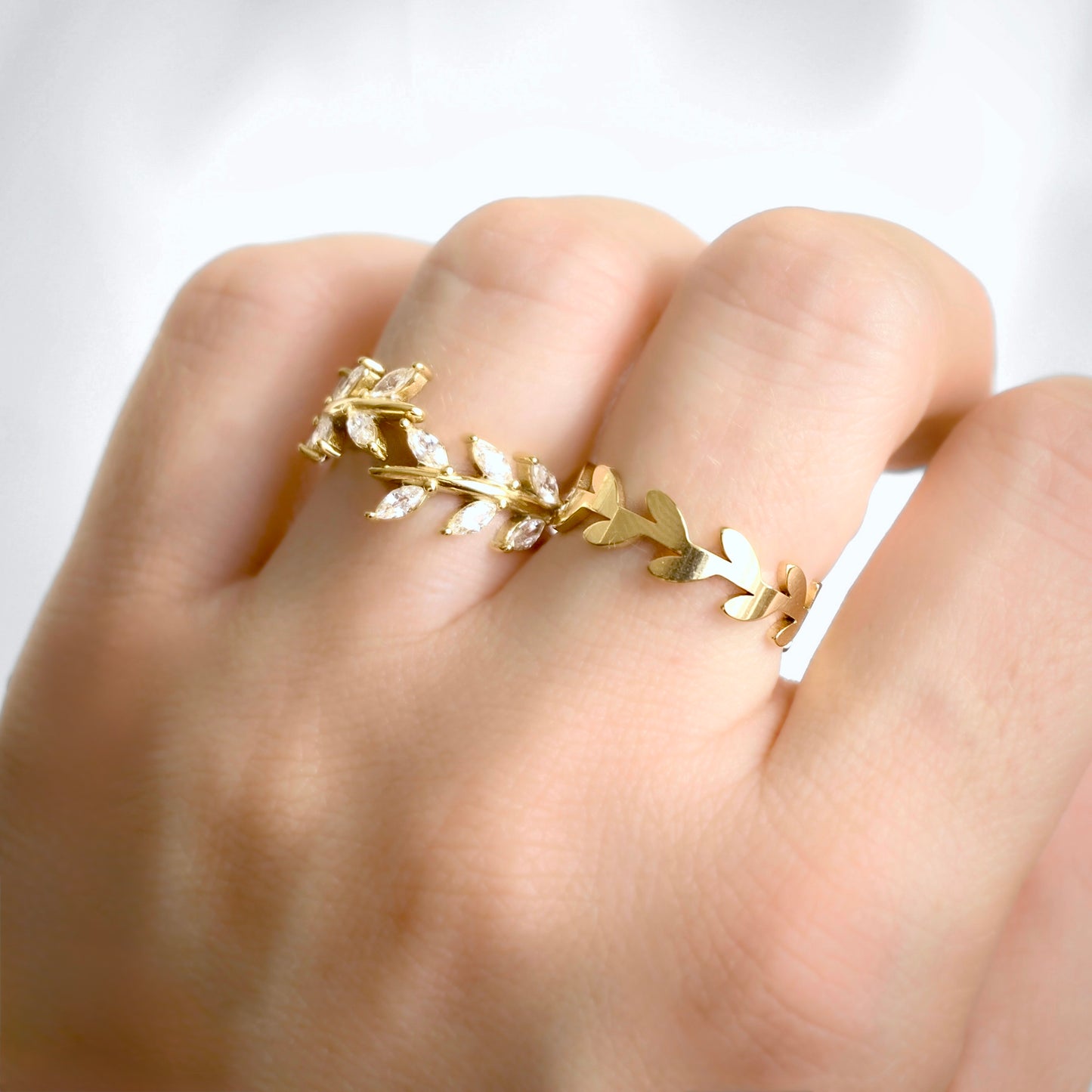 A gold leaf wreath ring worn on a person's finger, shown in a close-up lifestyle shot against a soft white background.