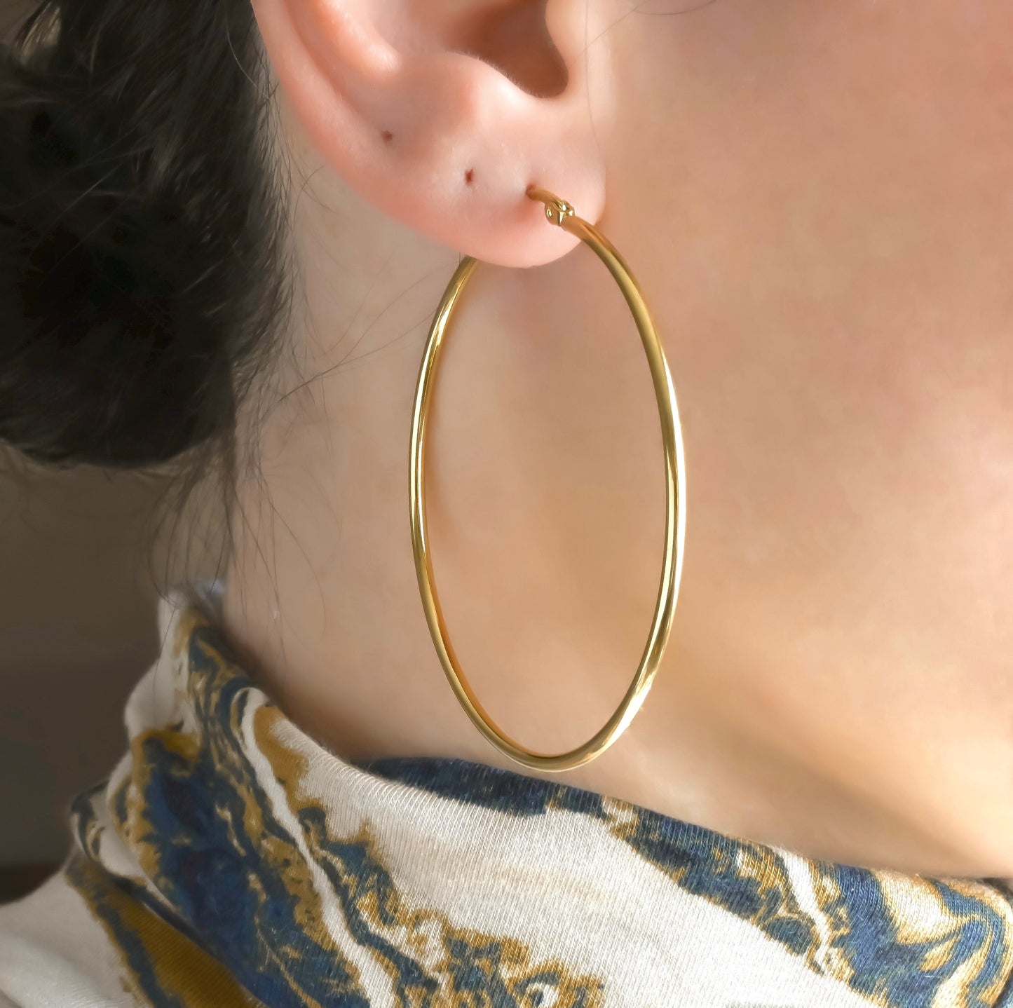 60mm oversized gold hoop earrings worn by a person with a blurred background