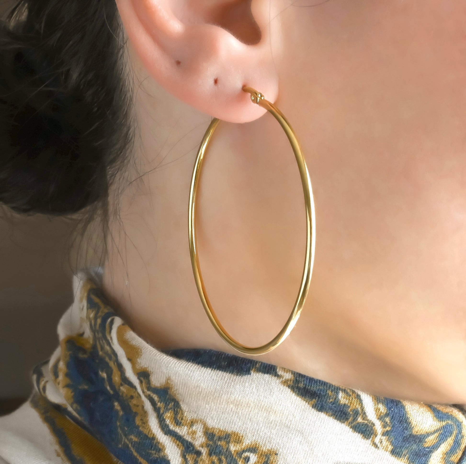 60mm oversized gold hoop earrings worn by a person with a blurred background