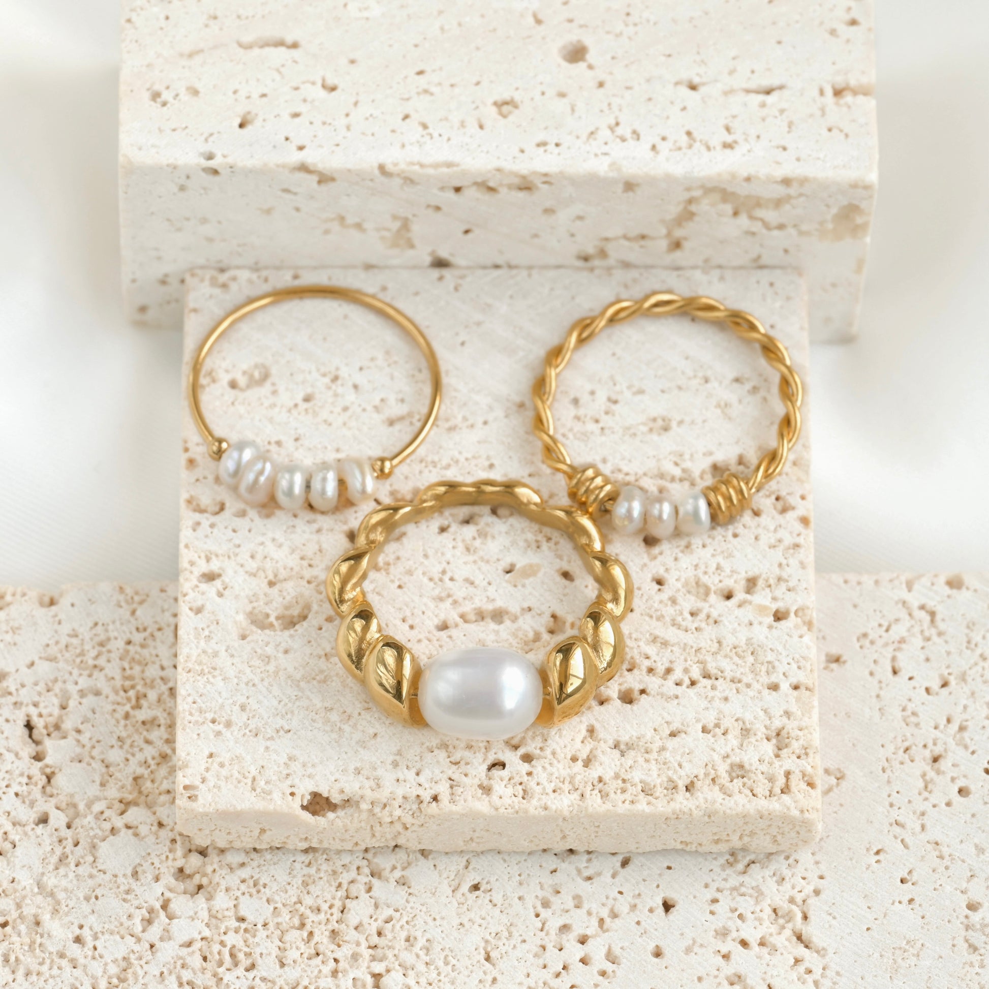 Top view of gold rings with pearls on a textured stone surface