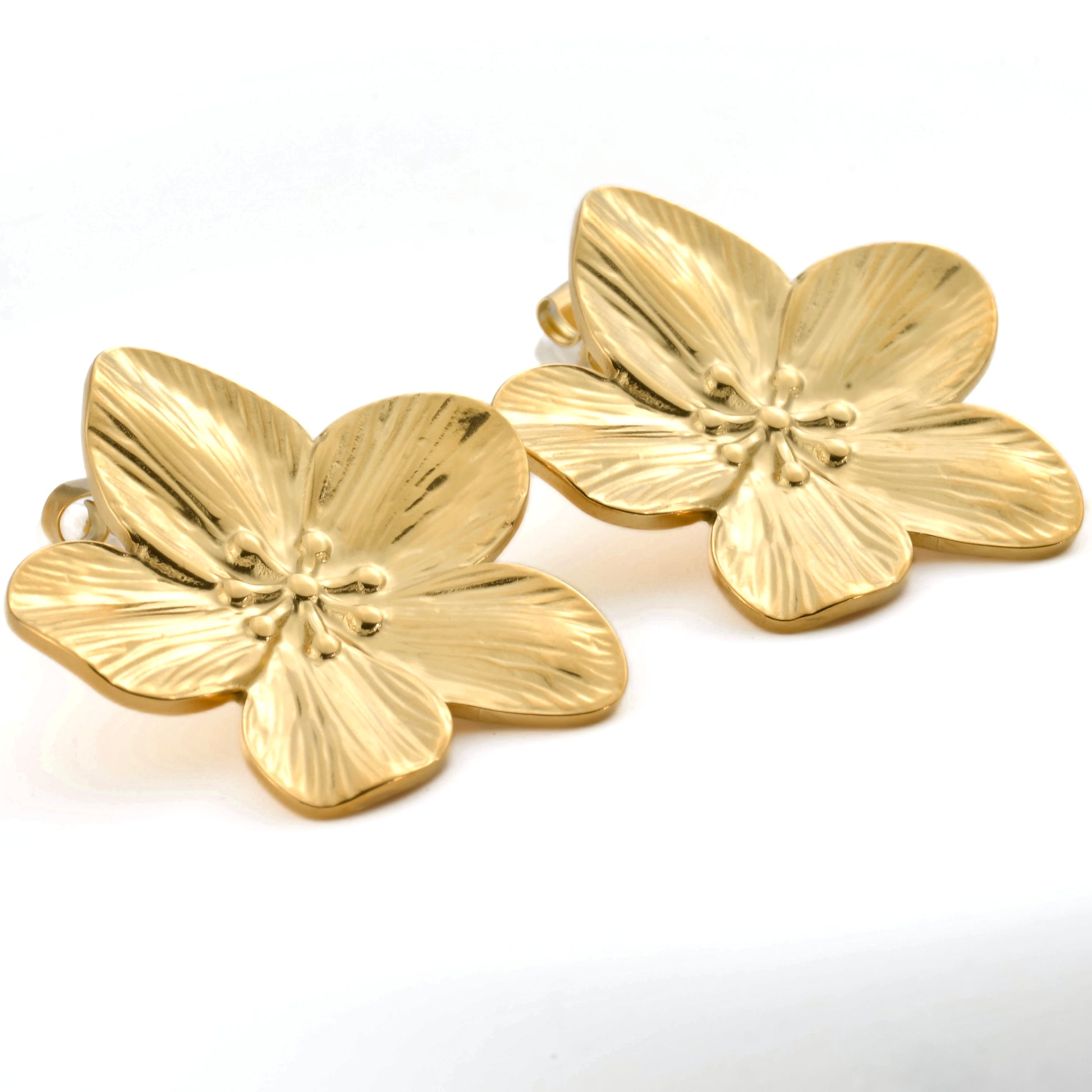 Pair of gold flower-shaped earrings on a white background from a different angle