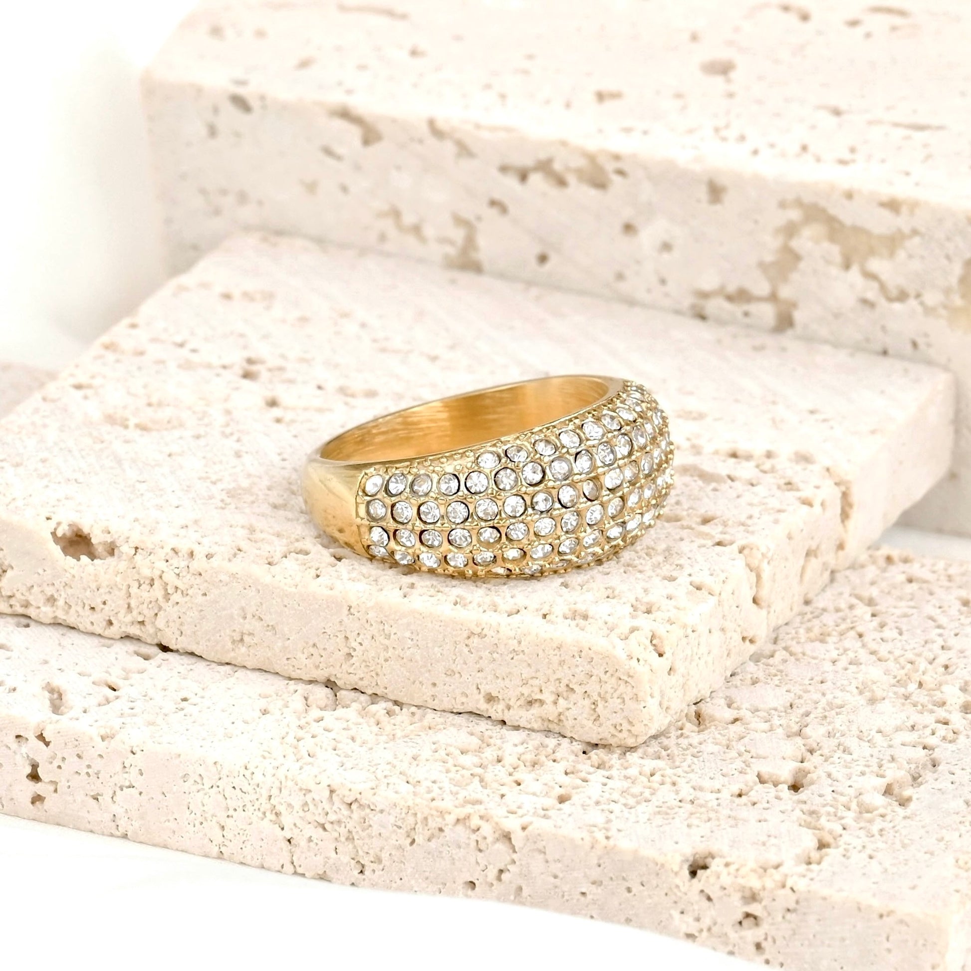 Chunky gold dome ring pave set with clear stones on a textured beige surface