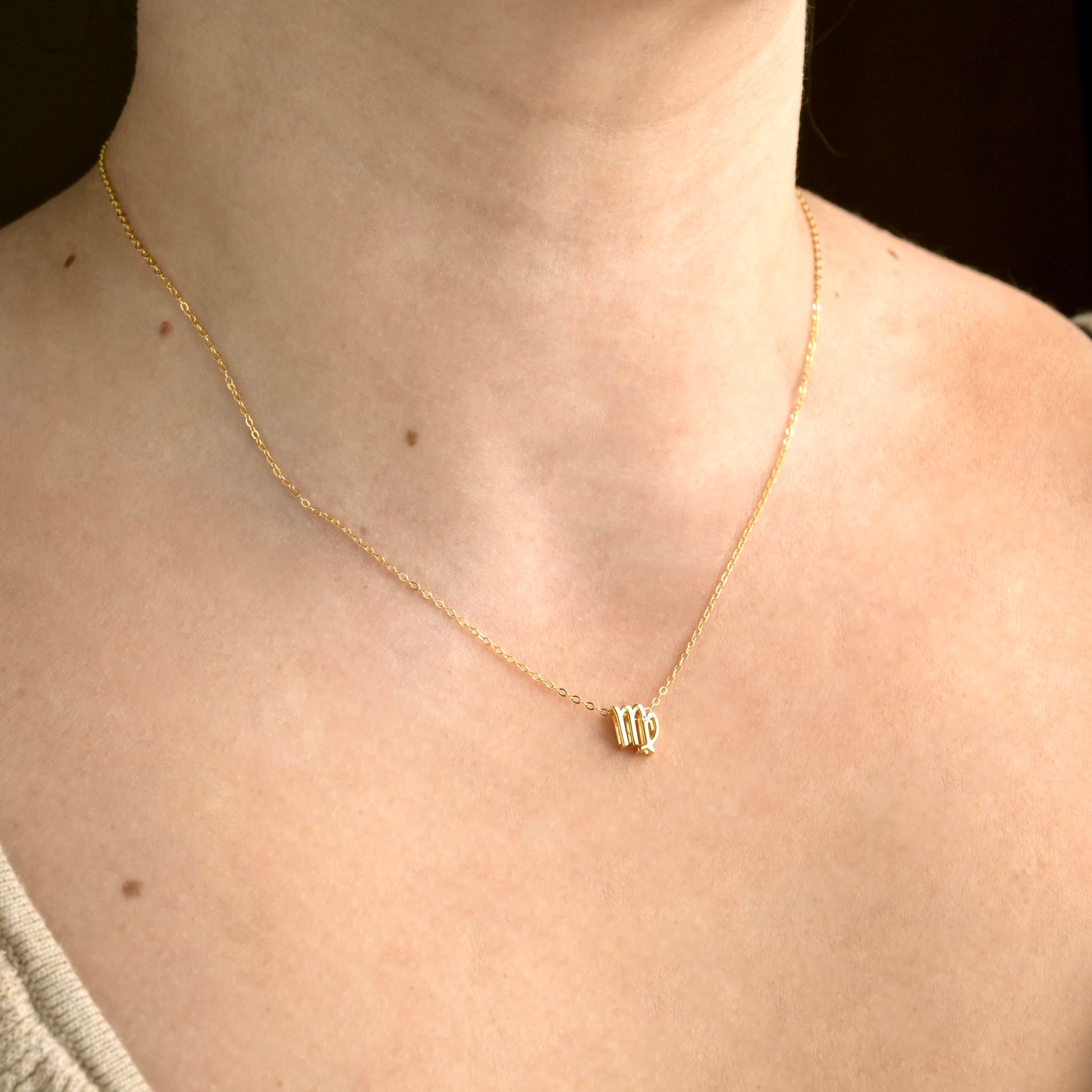 Gold necklace with virgo pendant on a person's neck against a dark background
