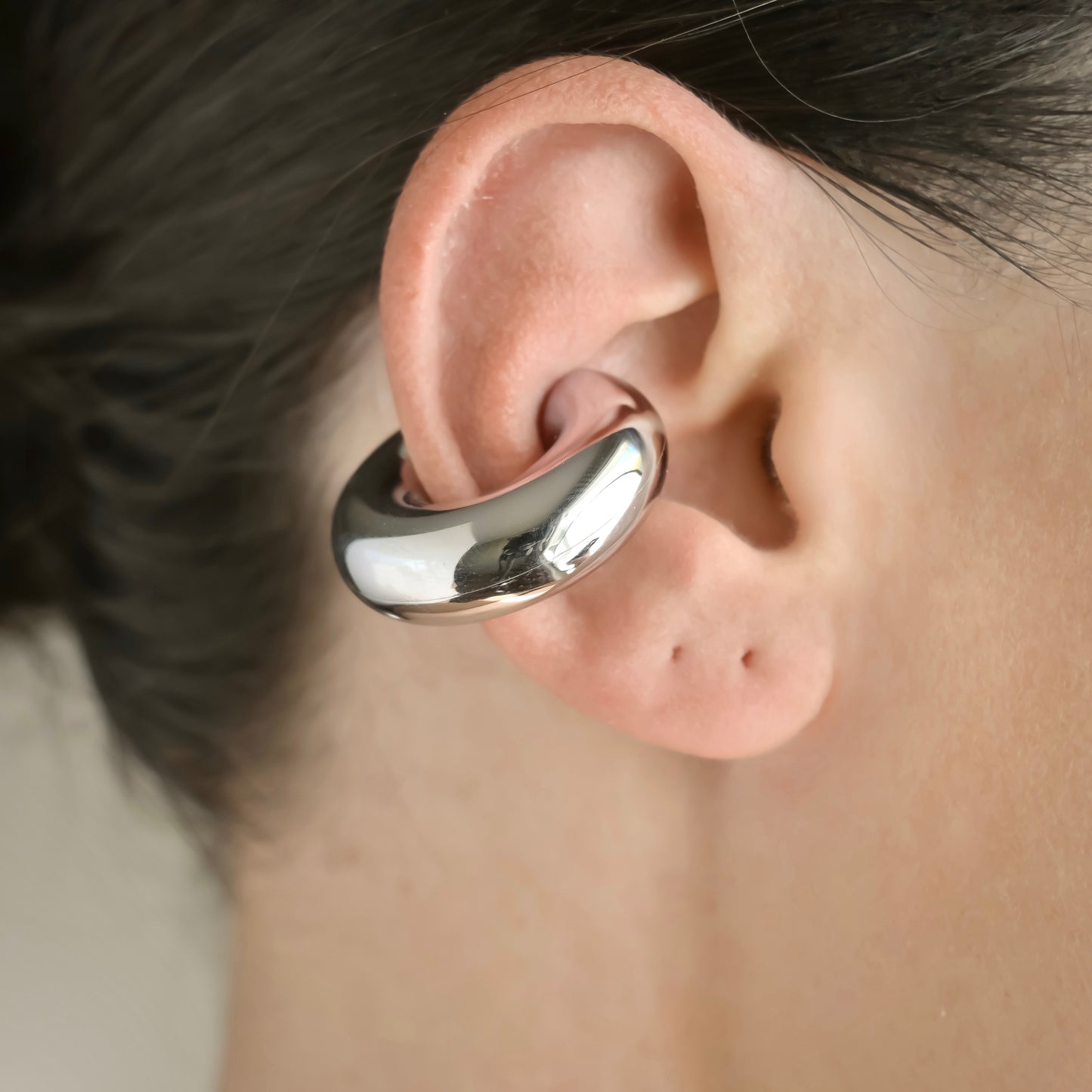 Close-up of a person wearing a oversized silver ear cuff.