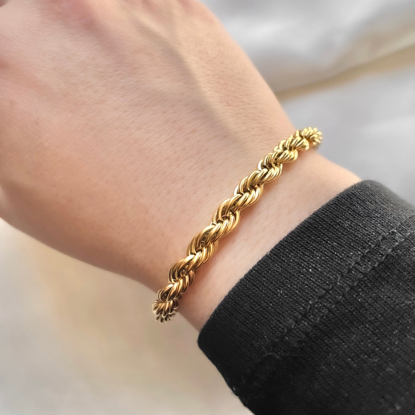 Gold rope bracelet on a wrist with a blurred background