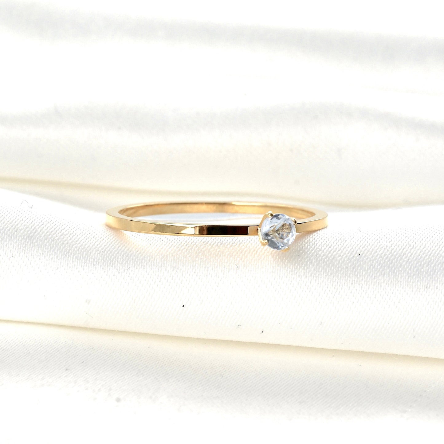 Gold solitaire ring with a clear CZ in a four prong setting on a white fabric background