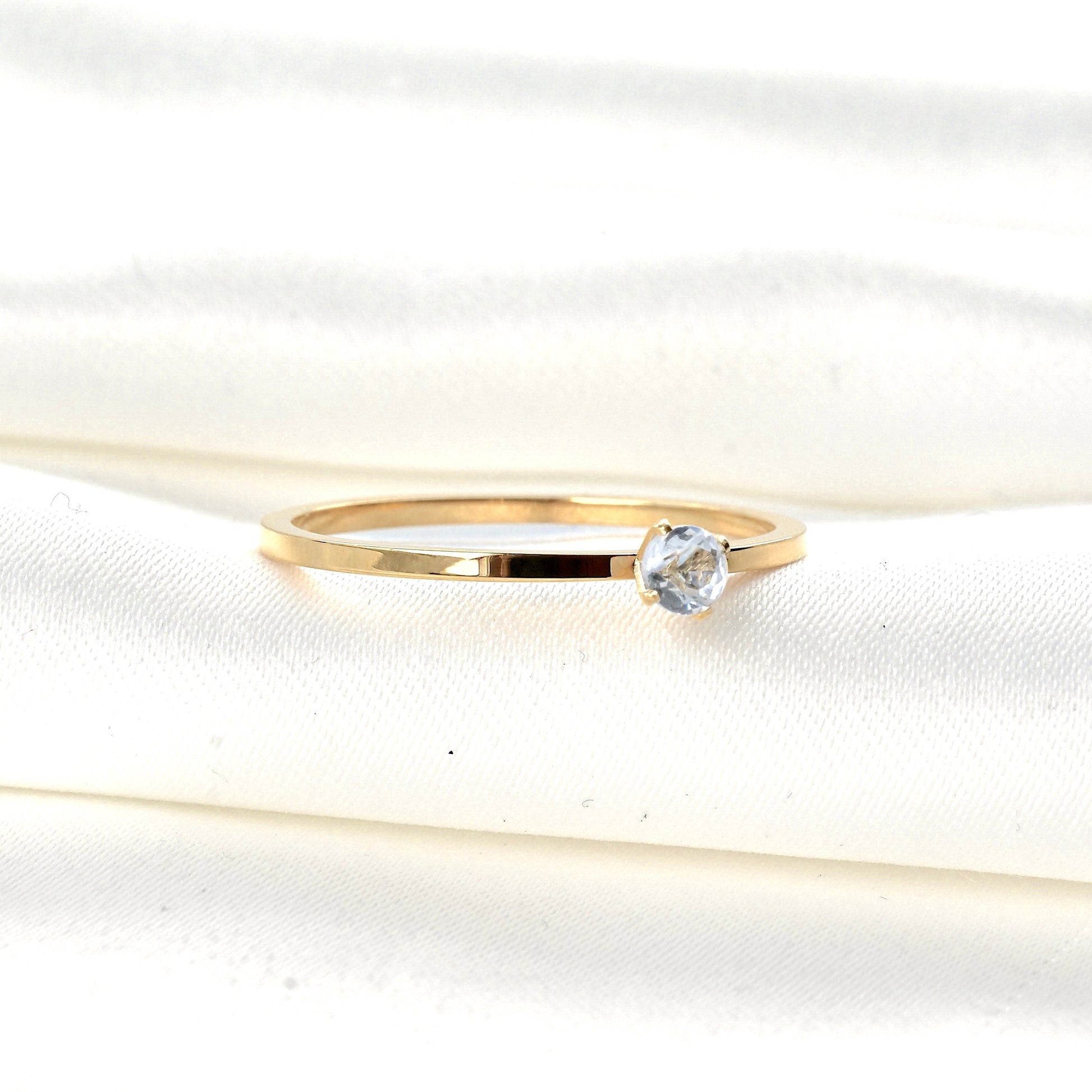 Gold solitaire ring with a clear CZ in a four prong setting on a white fabric background