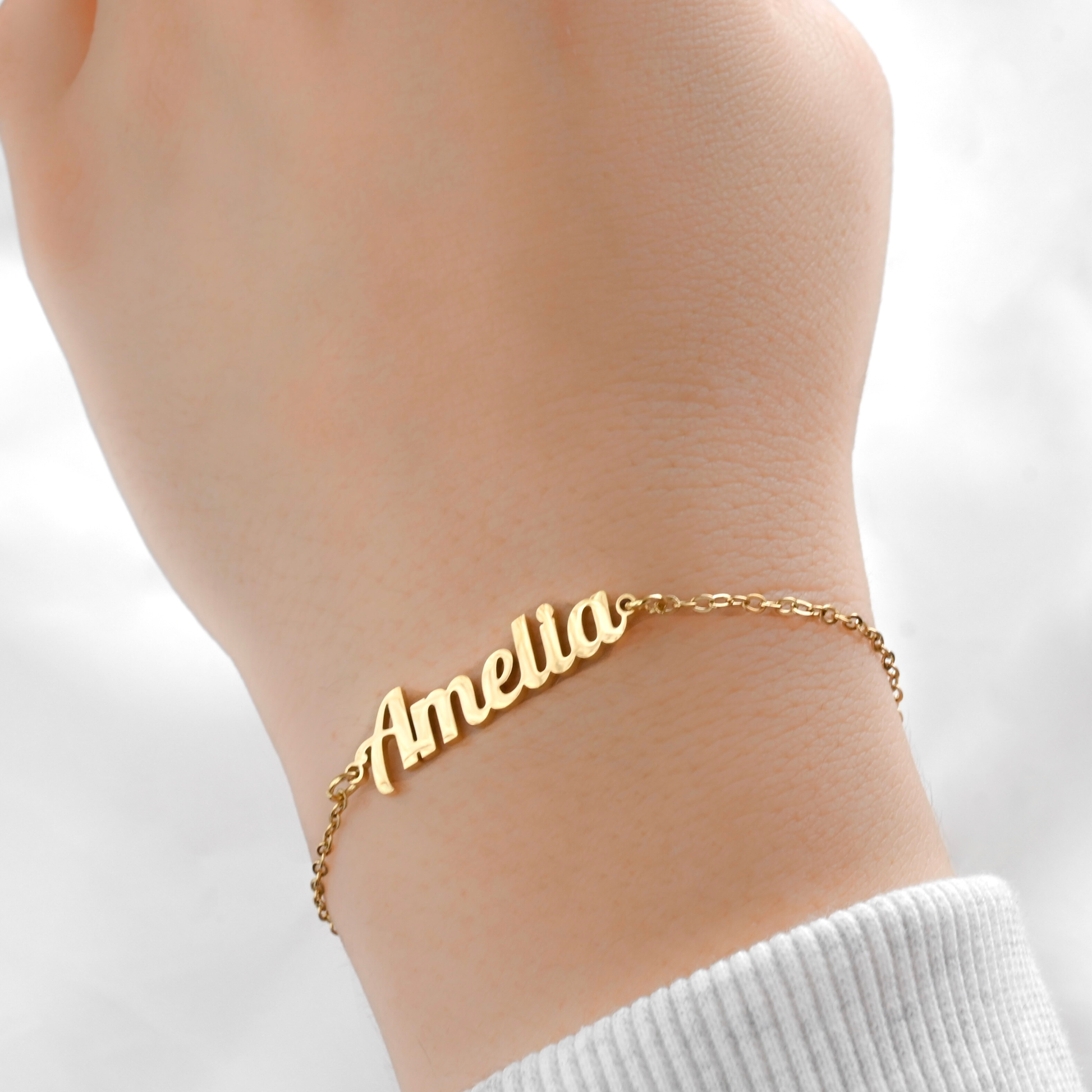 Gold name bracelet with 'Amelia' on a wrist against a white background