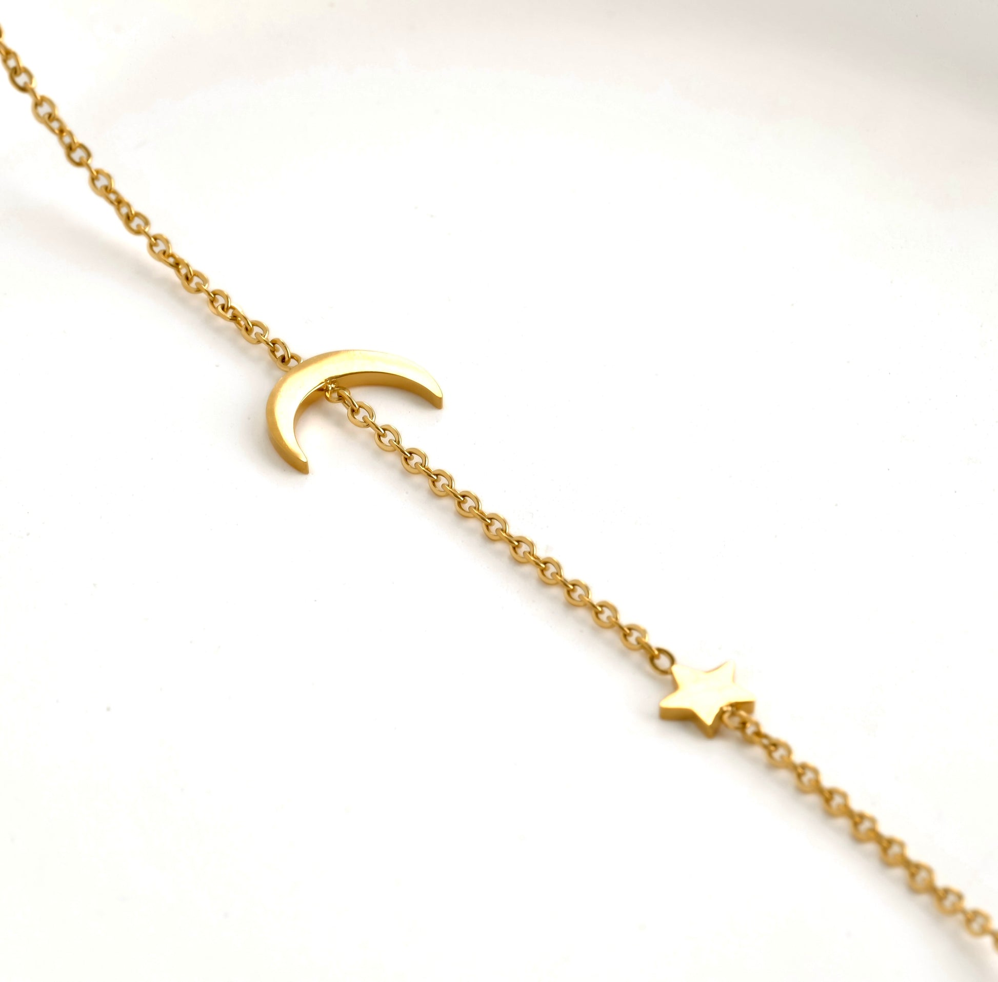 Gold bracelet with moon and star charms on a white background