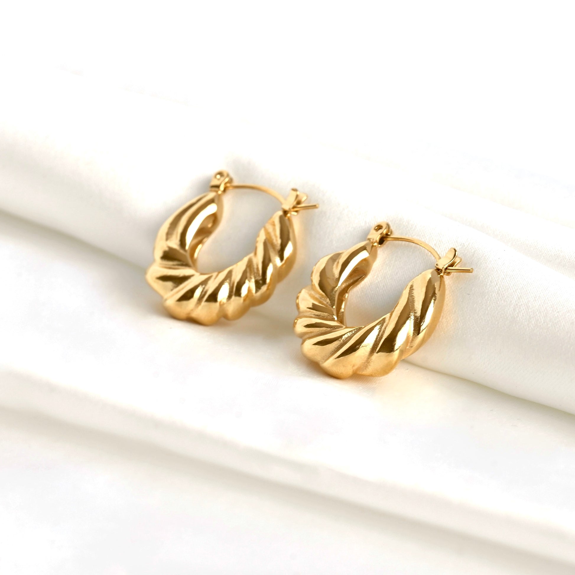 Angled view of medium gold twisted hoop earrings on a white surface