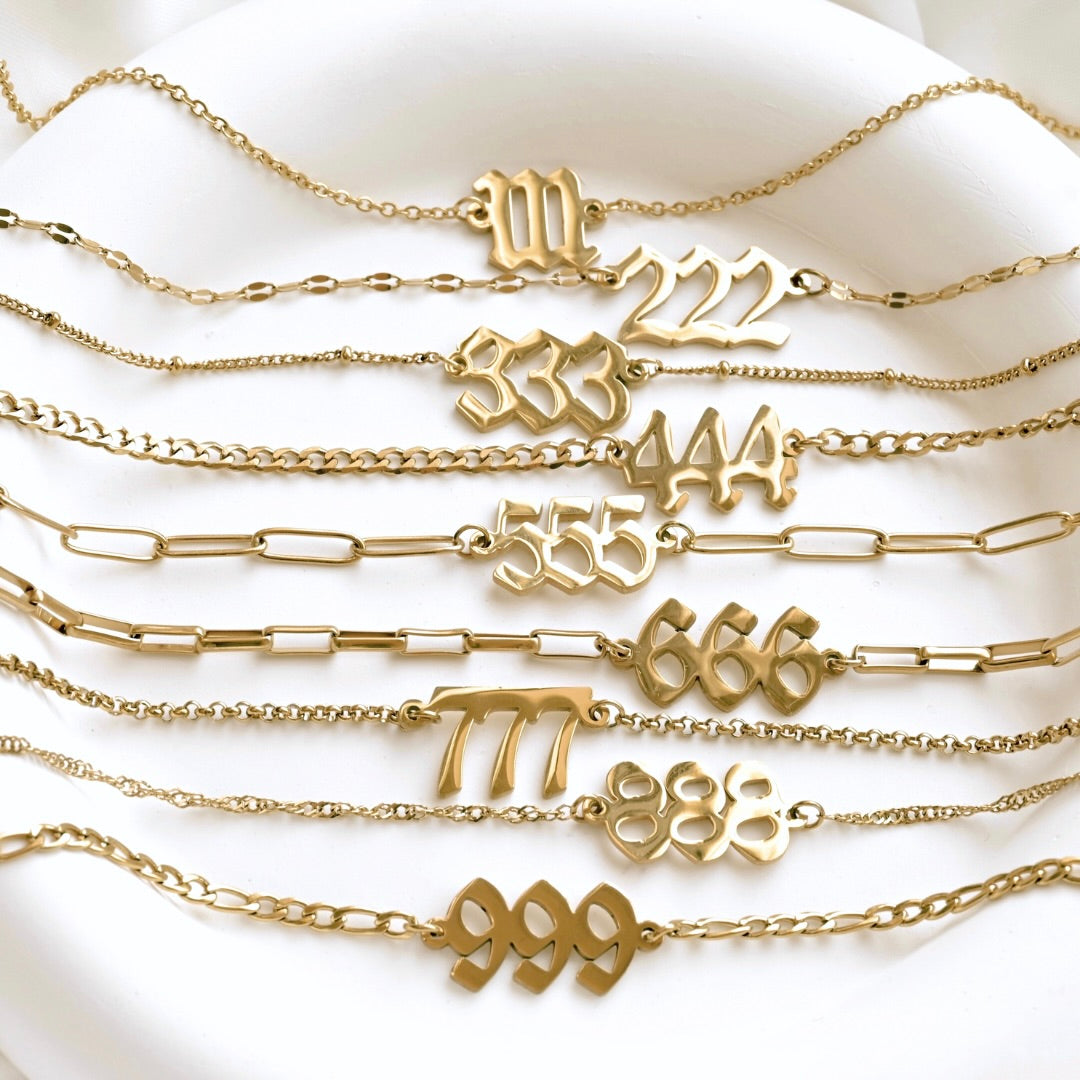 Gold necklaces with various angel number charms on a white surface