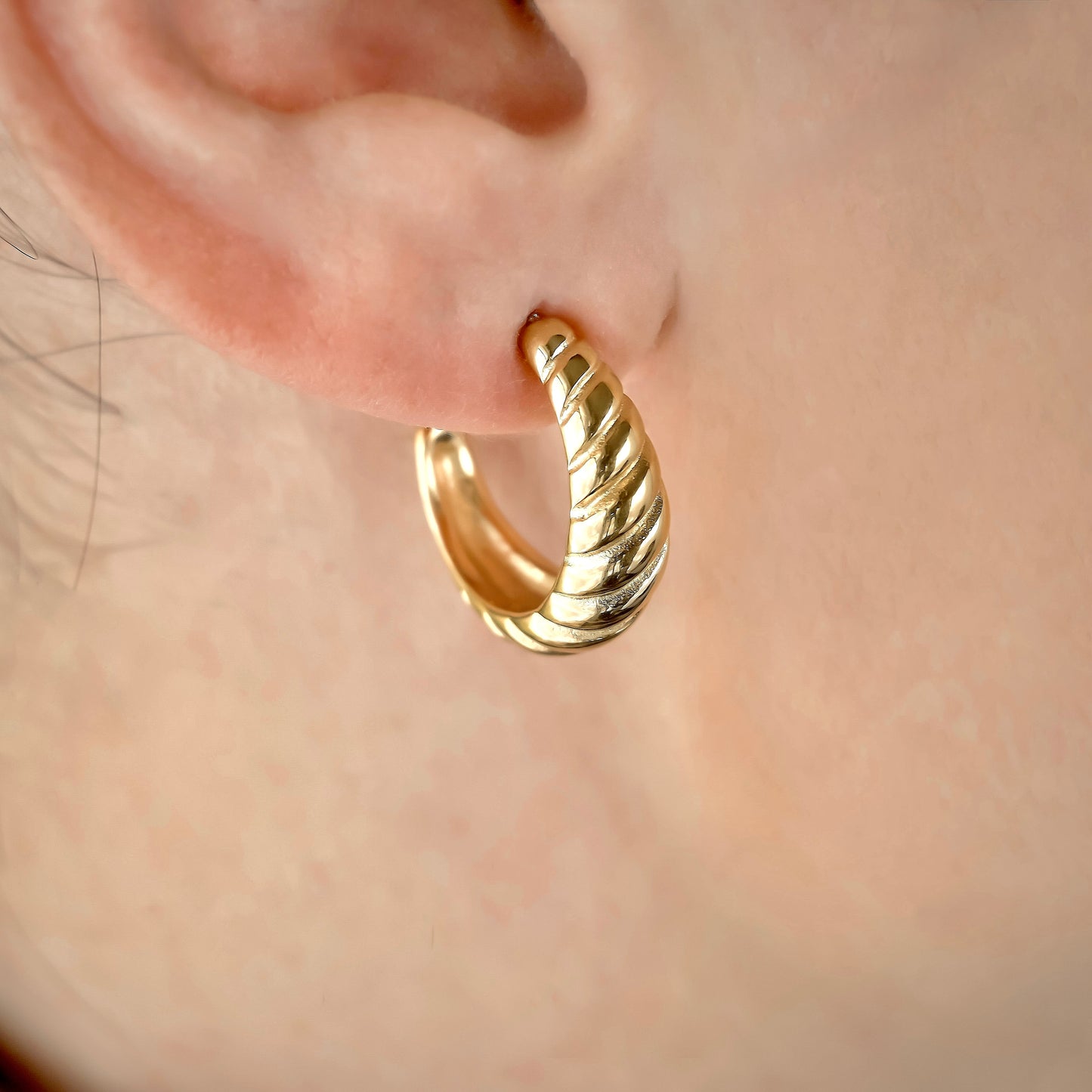 Gold twisted hoop earring worn on an ear with a blurred background