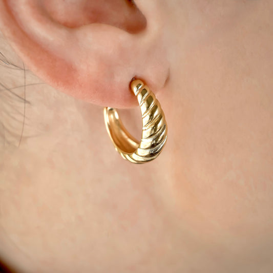 Gold twisted hoop earring worn on an ear with a blurred background