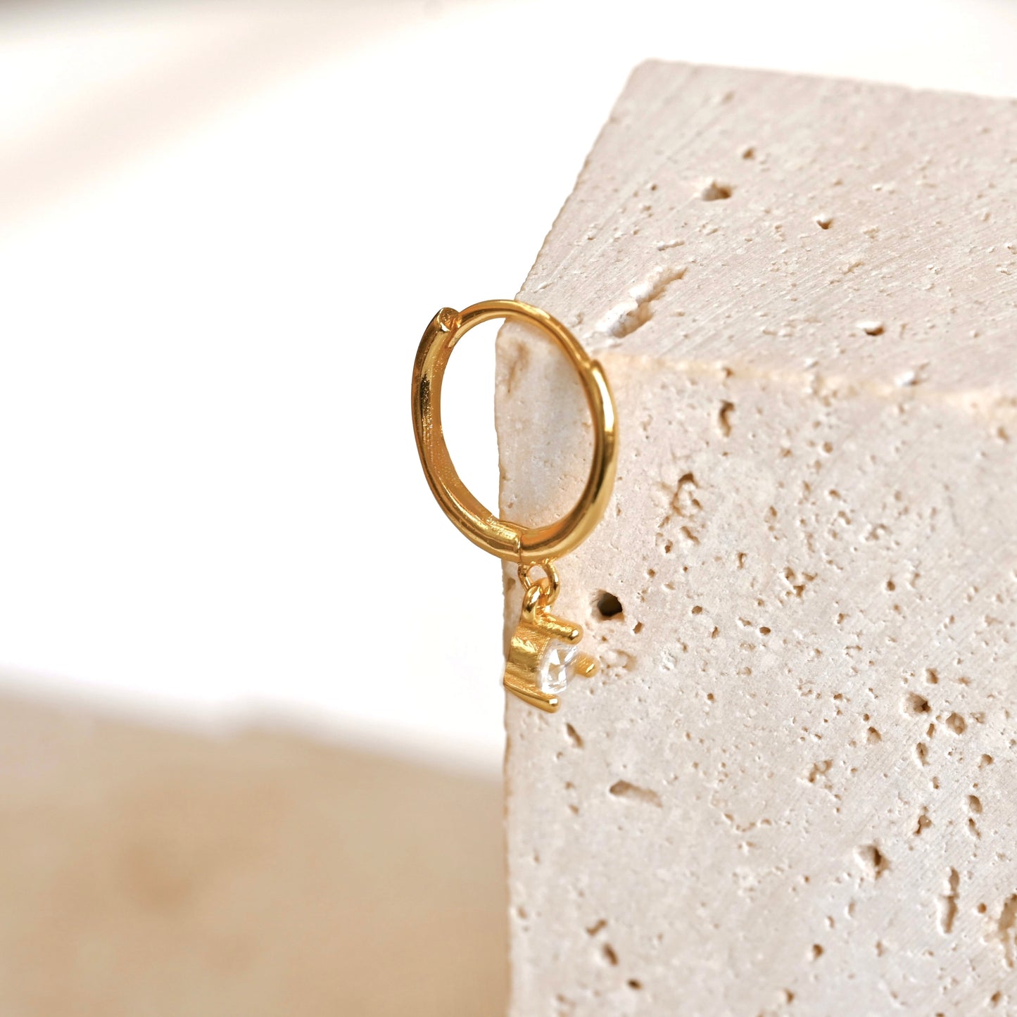 Mini gold clicker hoop earring on a textured beige stone
