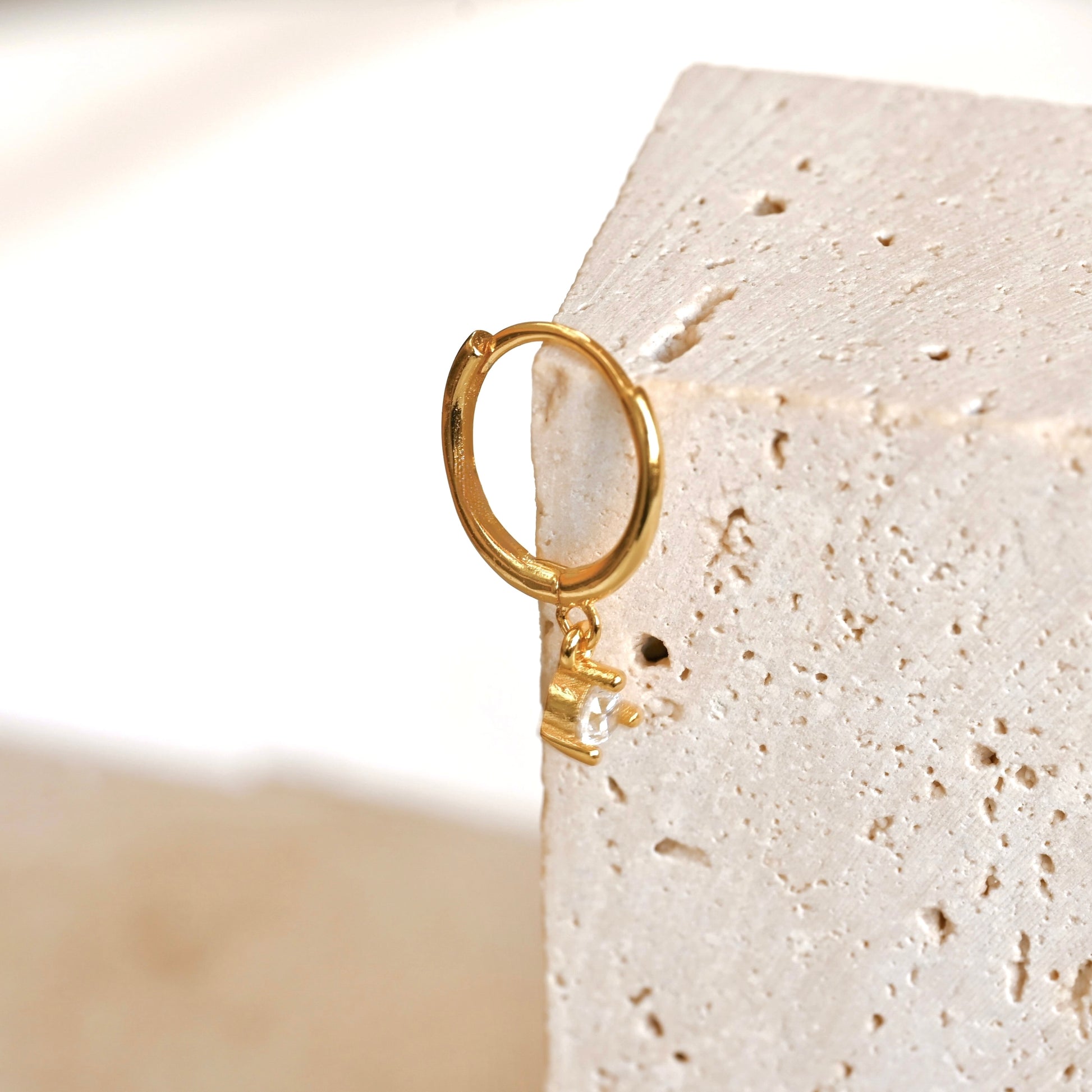 Mini gold clicker hoop earring on a textured beige stone