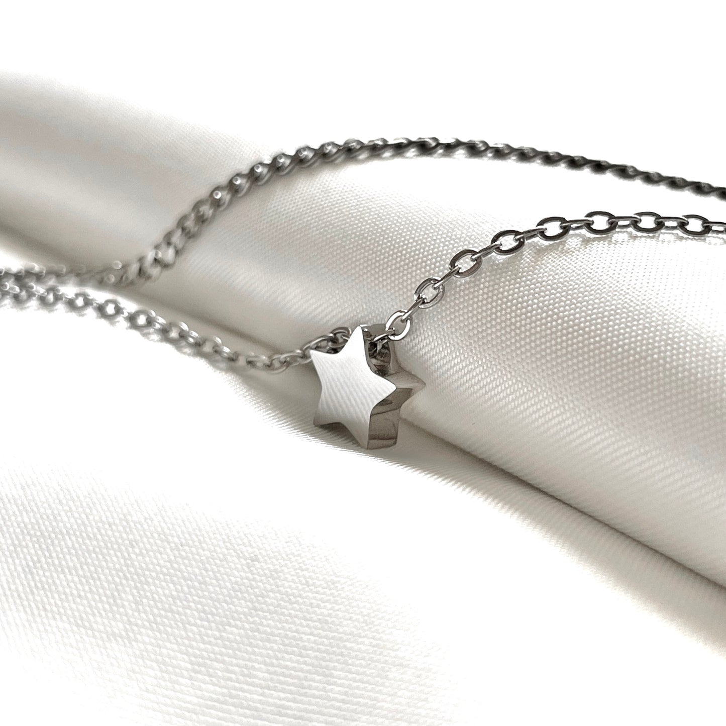 Silver star ankle bracelet on a white fabric background