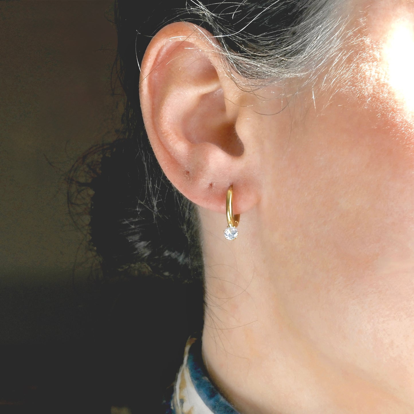 Close-up of an ear wearing a gold hoop earring with an attached round CZ