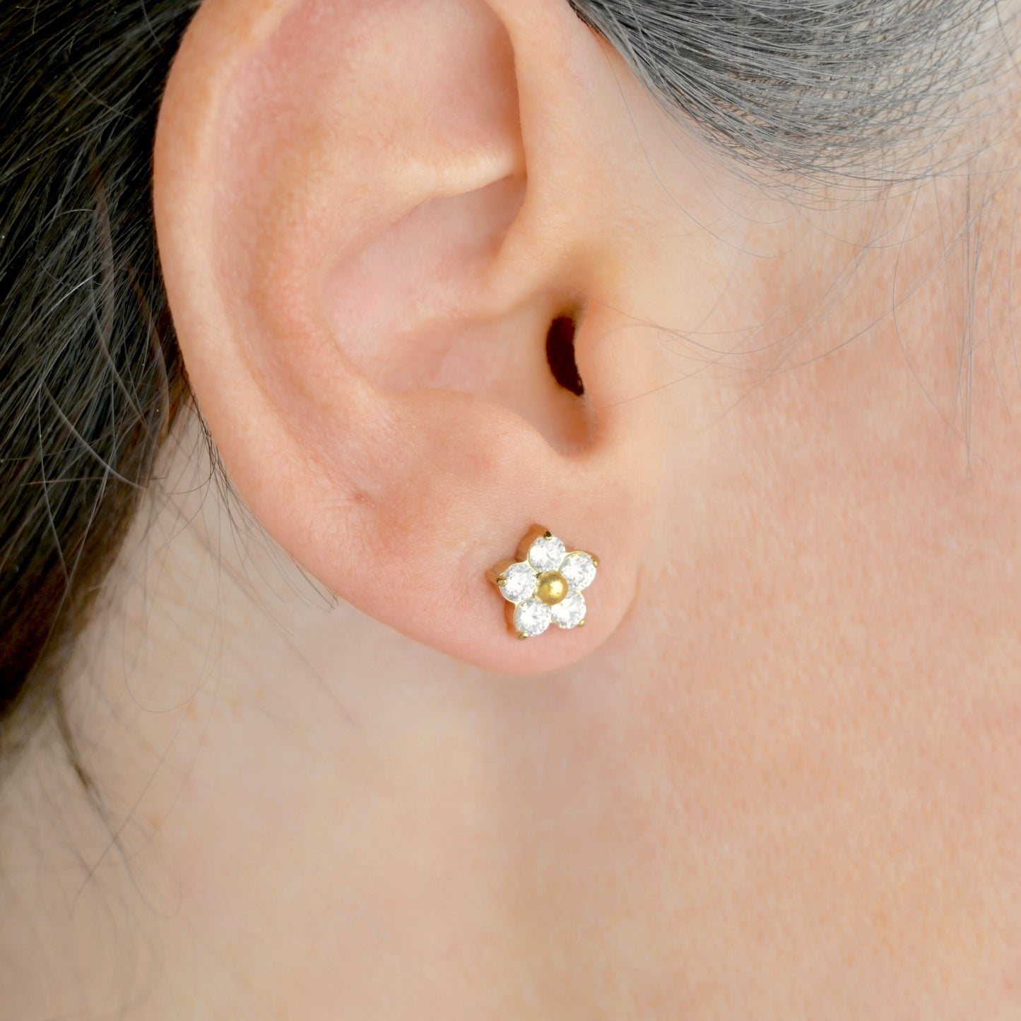 Close-up of an ear wearing a gold and white flower-shaped earring with clear CZ.