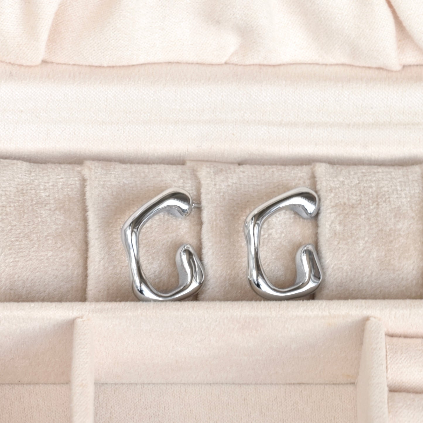 Silver earrings on a beige cushion