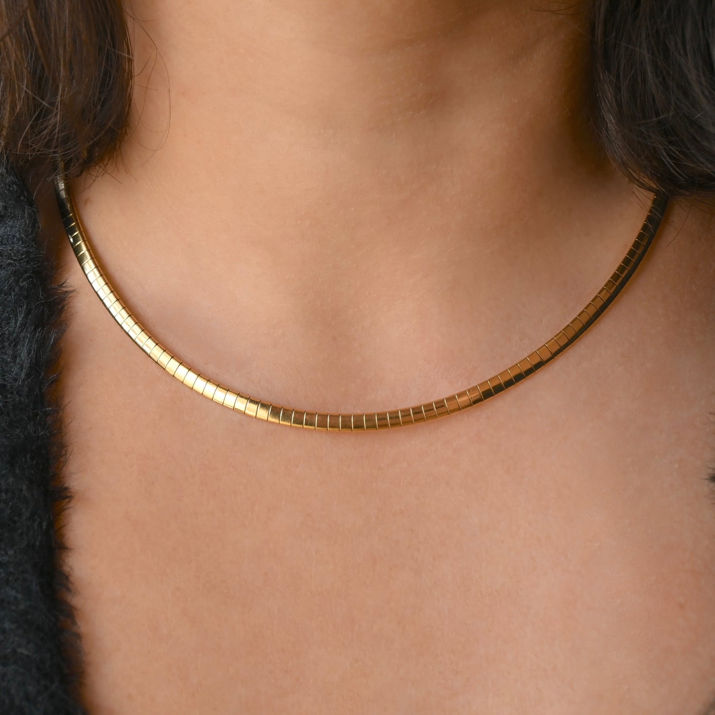 A close-up of a person's neck and upper chest wearing a thin, segmented gold chain necklace.
